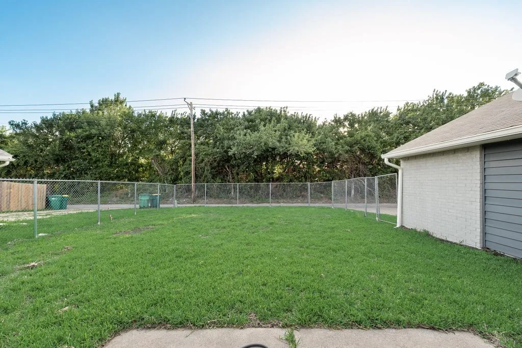 Expansive fenced yard featuring a concrete patio, green lawn, and chain-link perimeter