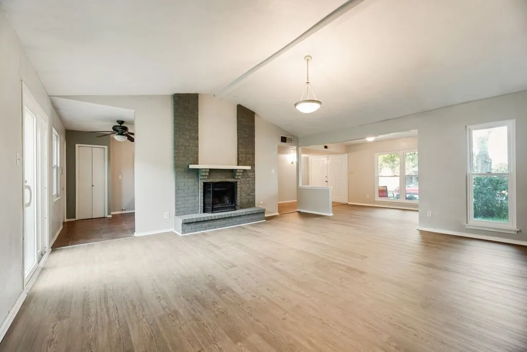 Spacious living area featuring wood-finish flooring, a vaulted ceiling, and a brick fireplace
