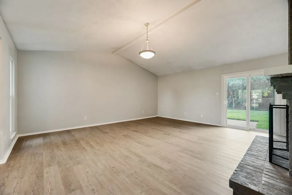 Spacious living area featuring vaulted ceilings, wood-finish flooring, and a stone fireplace with a black metal screen