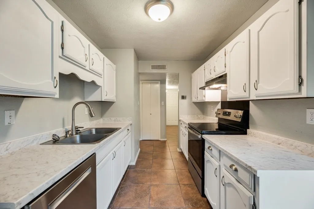 Galley kitchen featuring white cabinetry, light-colored countertops, a stainless steel double sink with a gooseneck faucet, a built-in dishwasher, and a black electric range with an overhead vent hood