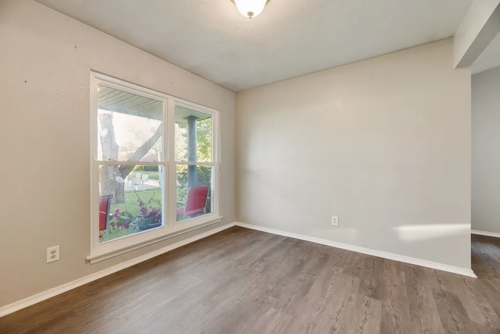 Neutral wall paint, wood-finish flooring, white baseboards, and a double window looking out to the yard