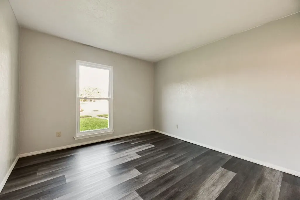 Room featuring dark wood-finish flooring, light neutral walls, and a white-framed window