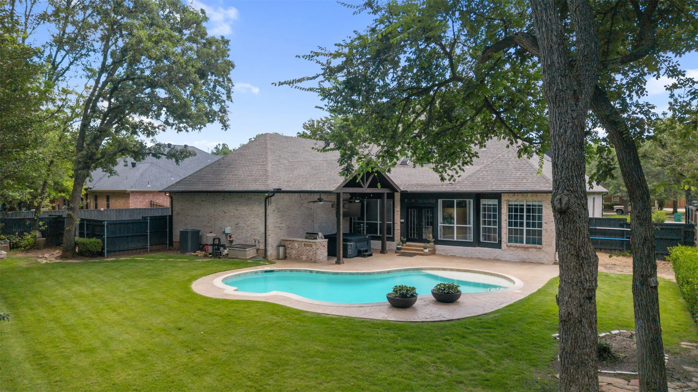 Spacious grassy backyard with lots of trees, pool and outdoor living center.