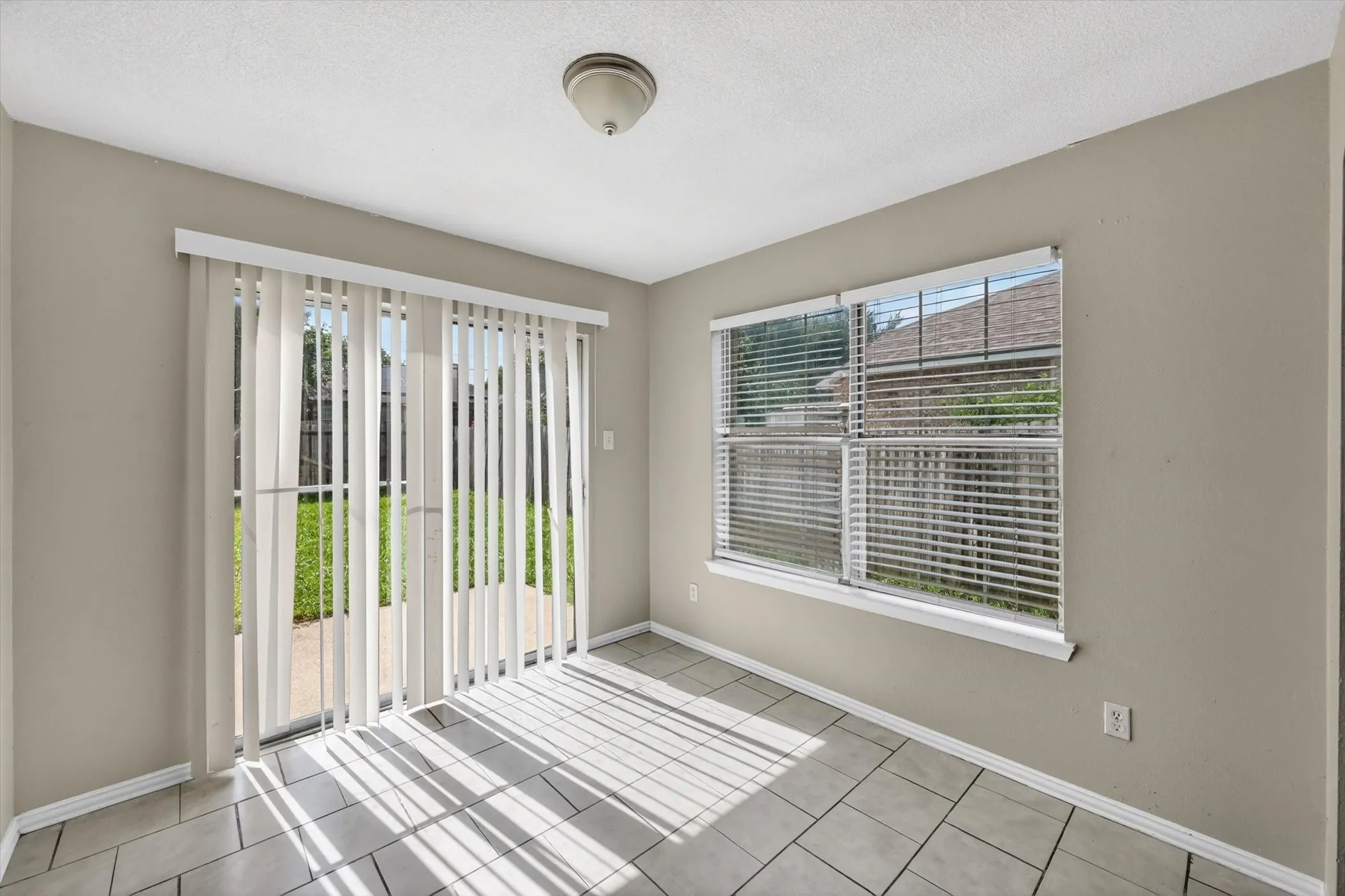 Dining area with ceramic tile flooring, a sliding glass door with vertical blinds, and a large window featuring horizontal blinds