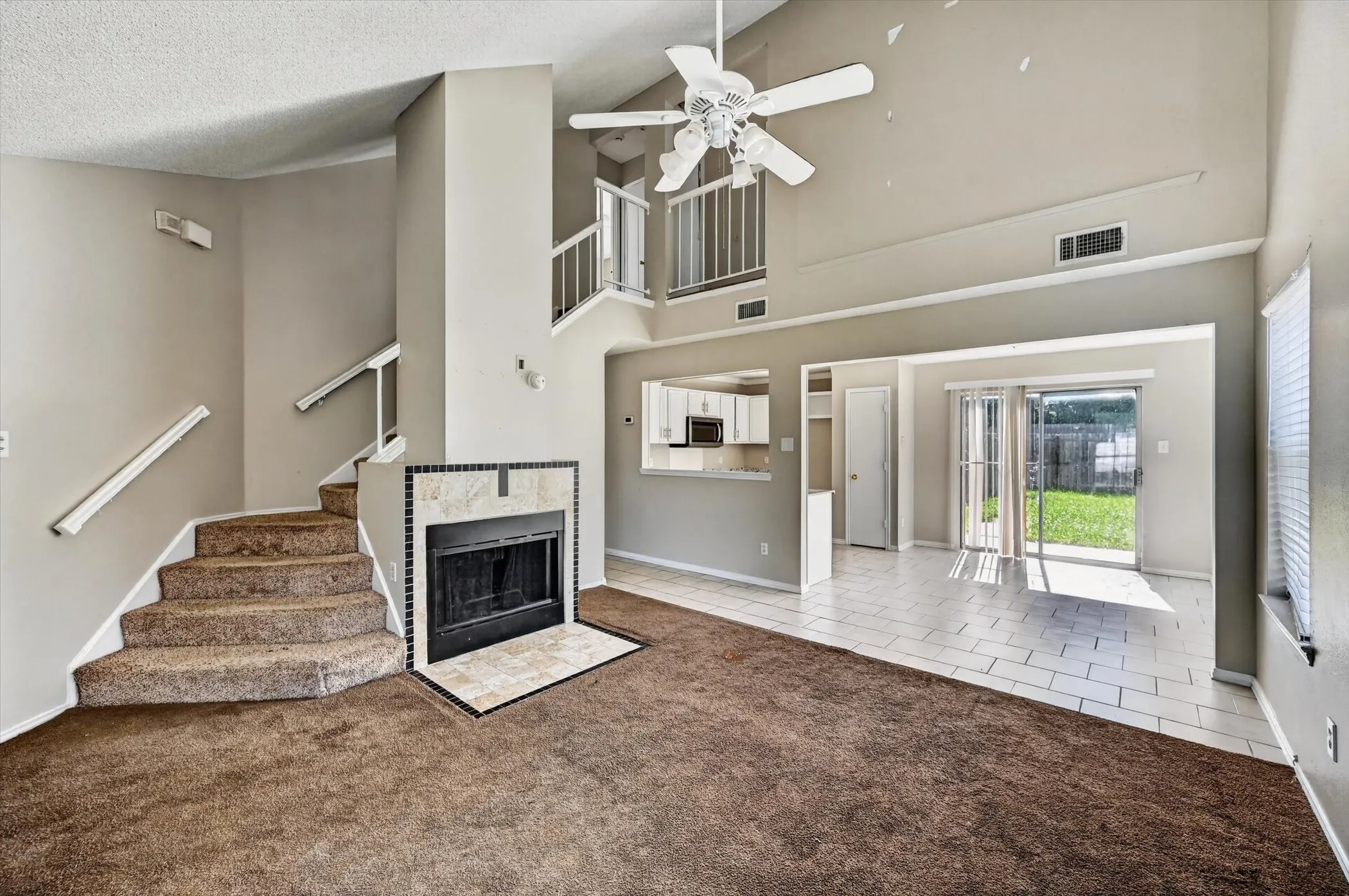 Vaulted ceiling living space with a ceiling fan, fireplace featuring a tiled surround and hearth, carpeted flooring, and a sliding glass door opening to a private exterior space