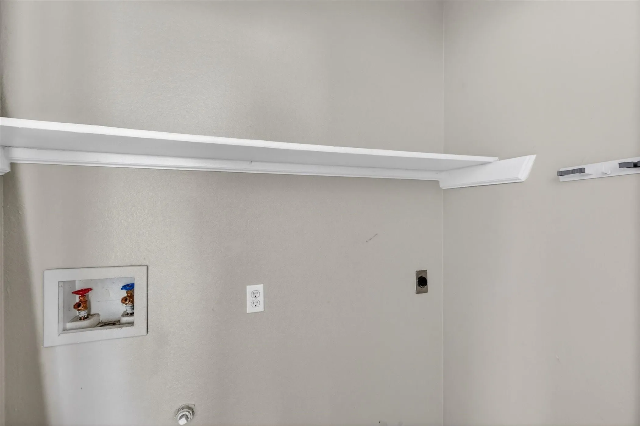 White shelving unit over a laundry hookup with hot and cold water valves