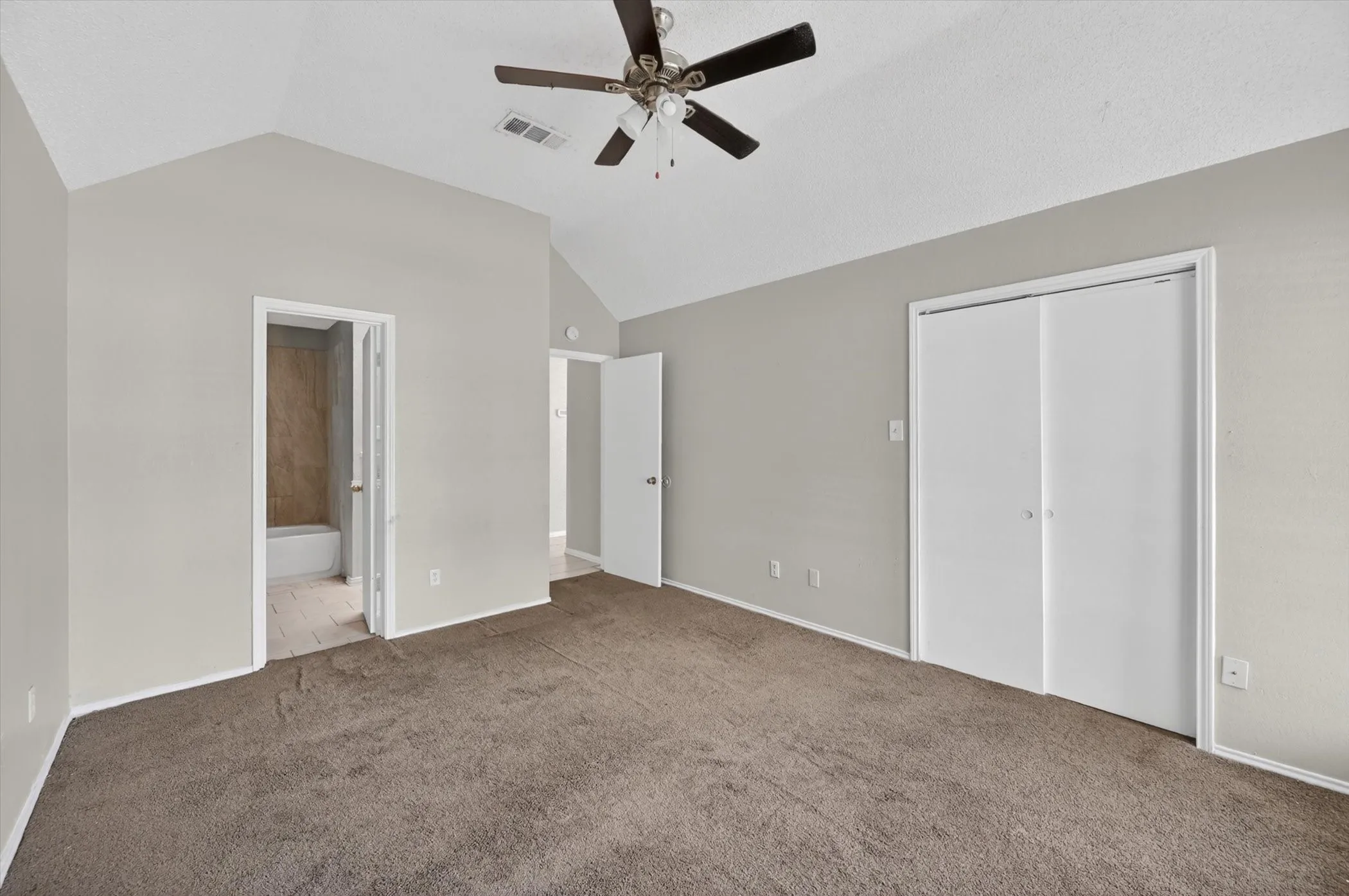 Spacious room with vaulted ceilings and a ceiling fan, featuring plush brown carpeting, light gray wall paint, and white trim