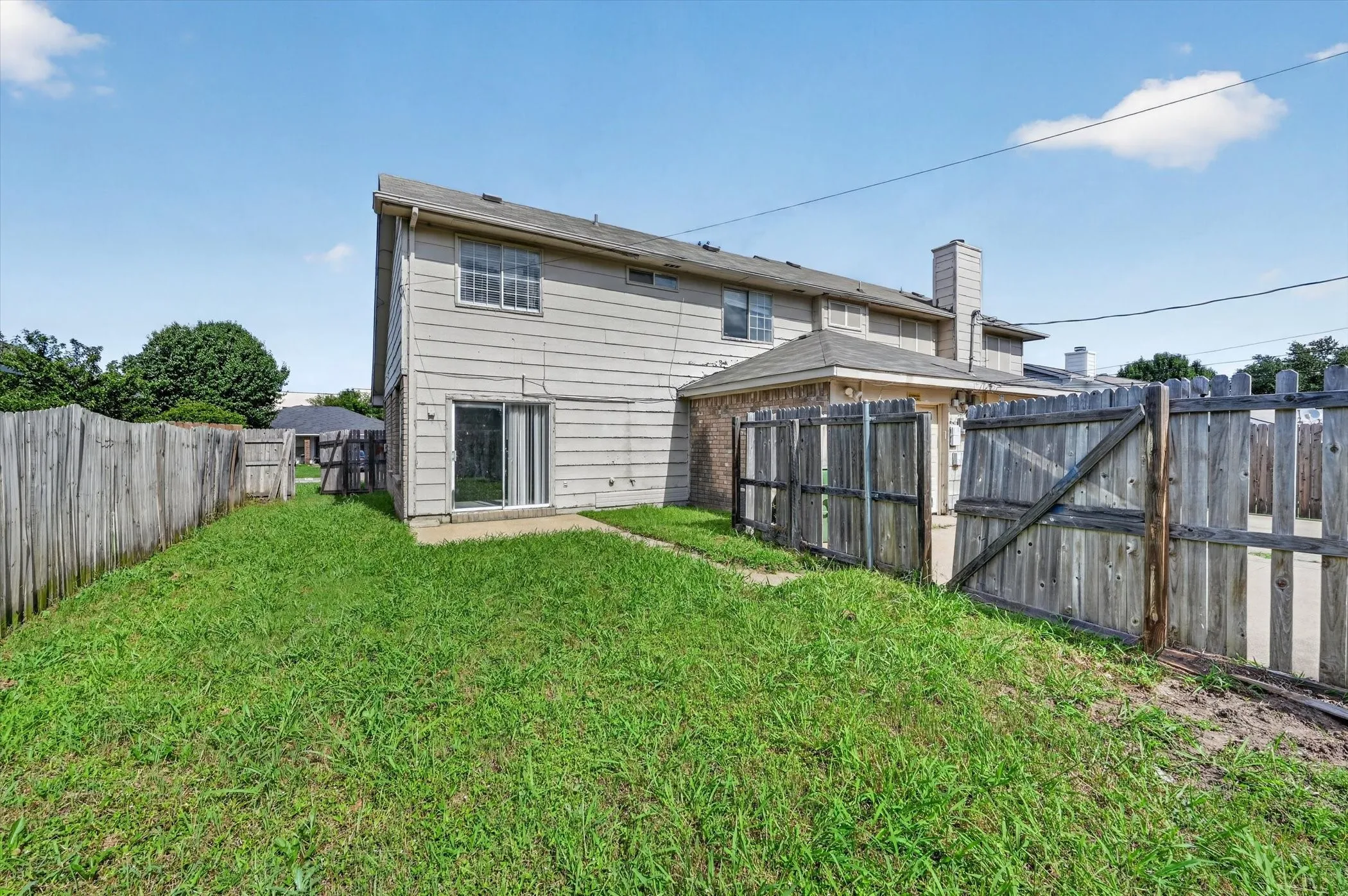 Expansive rear yard featuring a grass lawn, privacy fencing, and a concrete patio with sliding glass door access