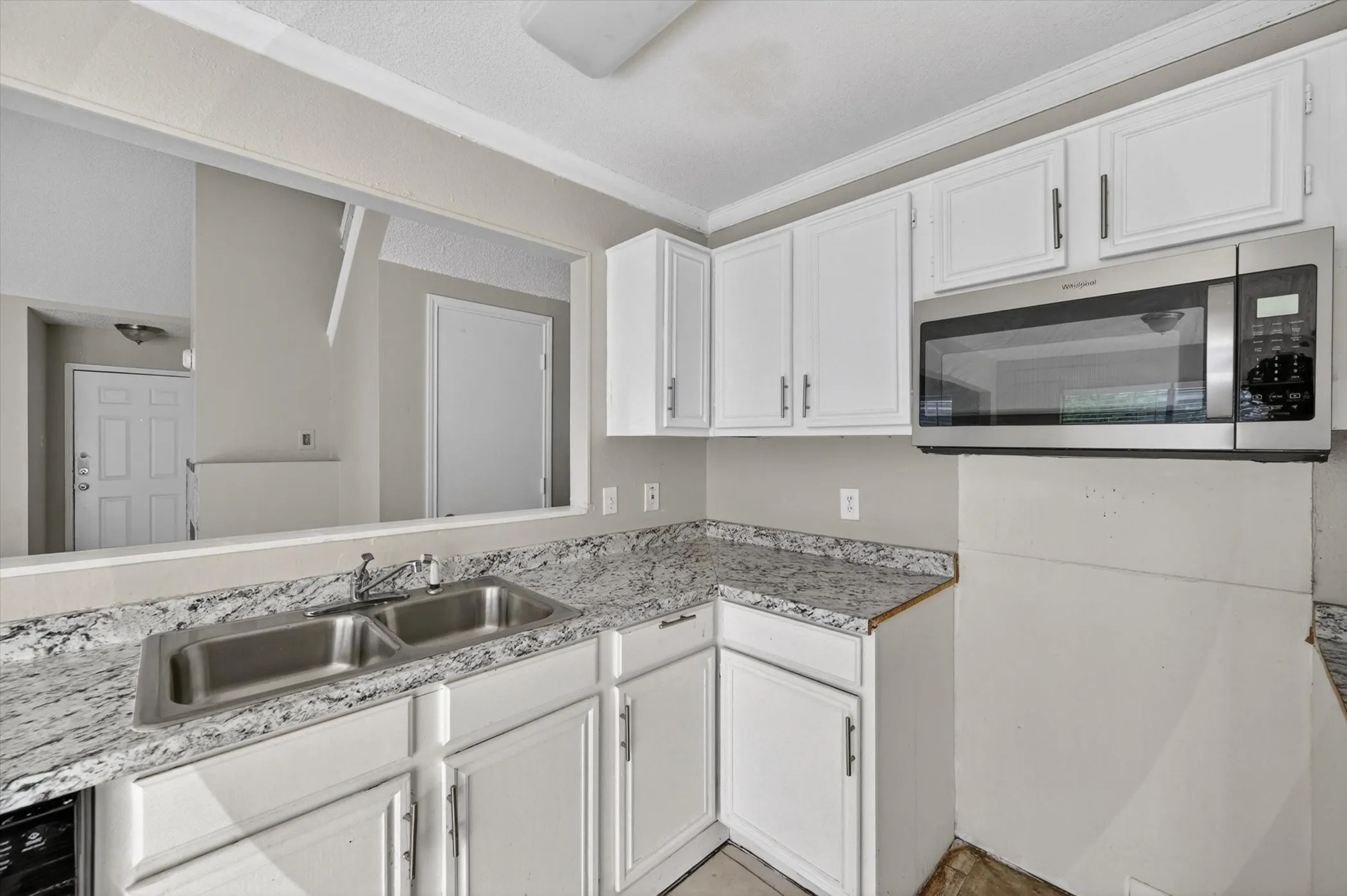 Kitchen featuring white cabinetry, a double basin stainless steel sink, a stainless steel microwave, and speckled countertops