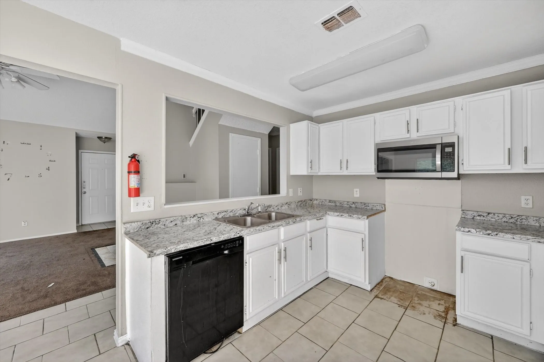 Kitchen featuring white cabinetry, light-toned countertops, a built-in microwave, a stainless steel double basin sink, and tile flooring