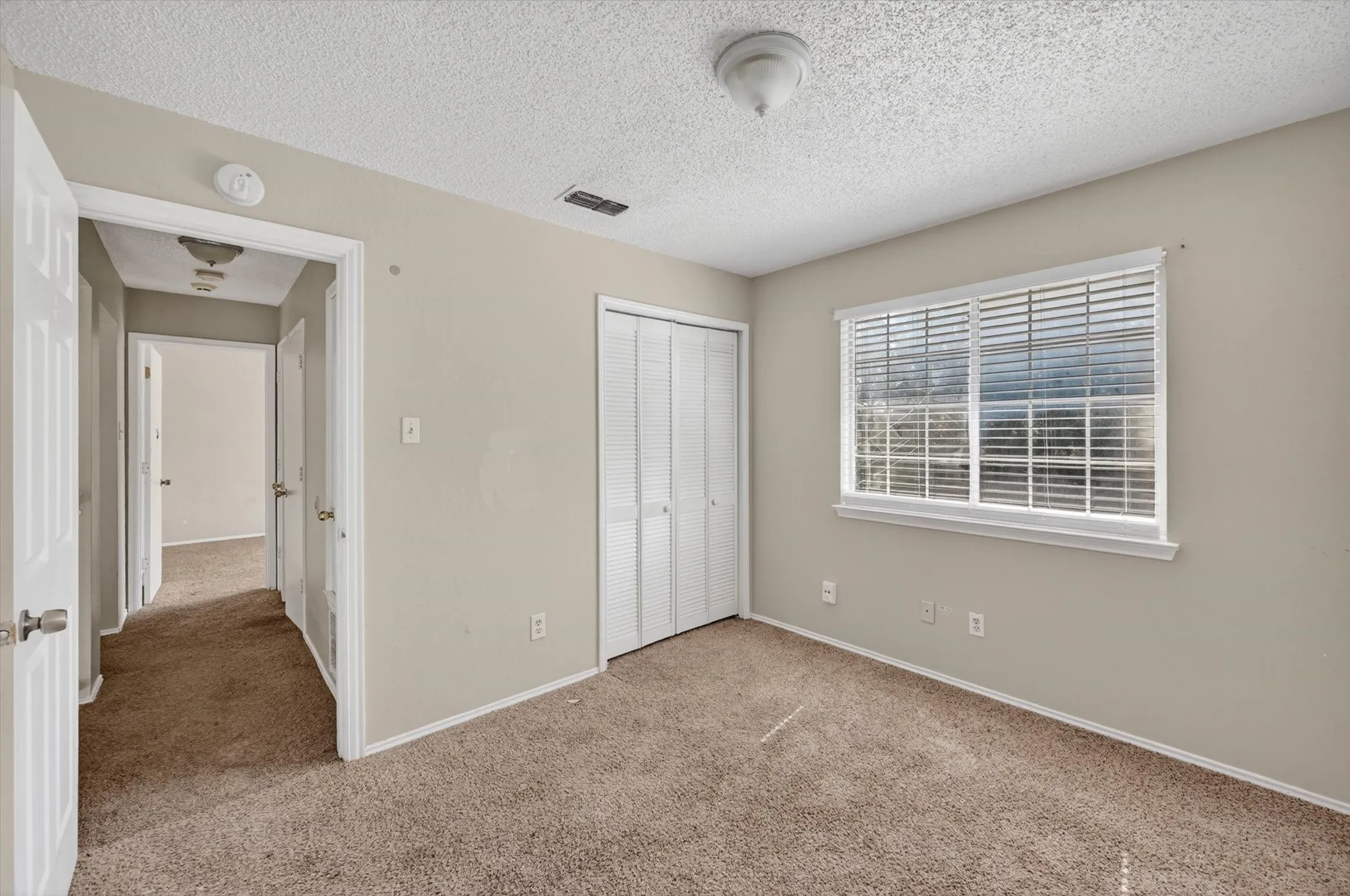 Room featuring a single window with blinds, bi-fold closet doors, wall-to-wall carpeting, and a ceiling-mounted light fixture