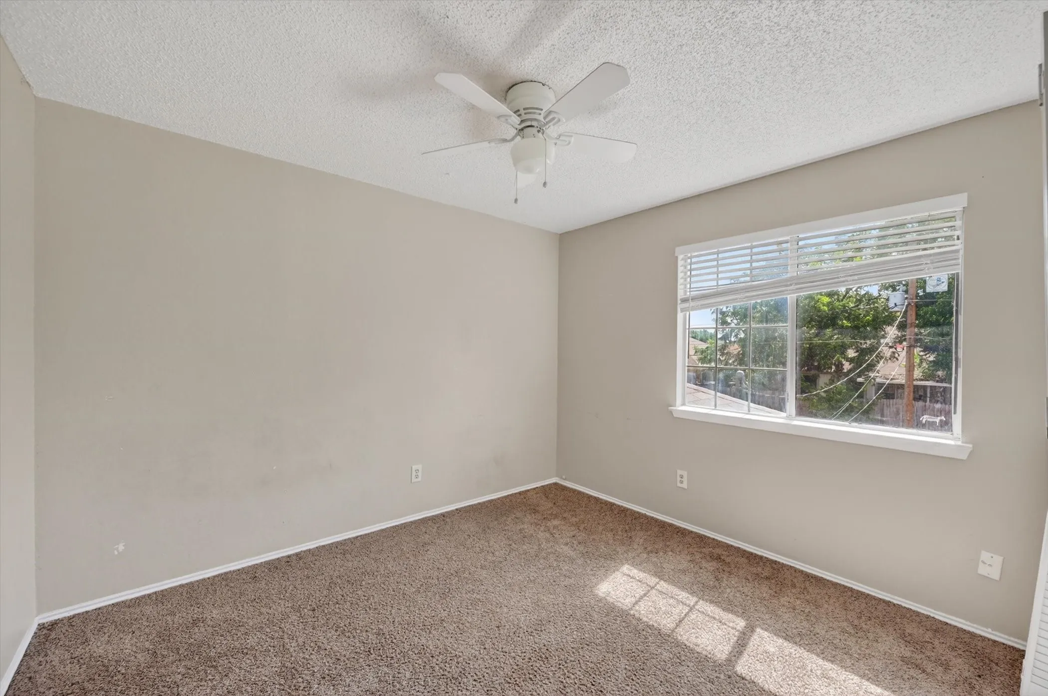 Carpeted room featuring a ceiling fan, a window with blinds, and neutral-toned walls