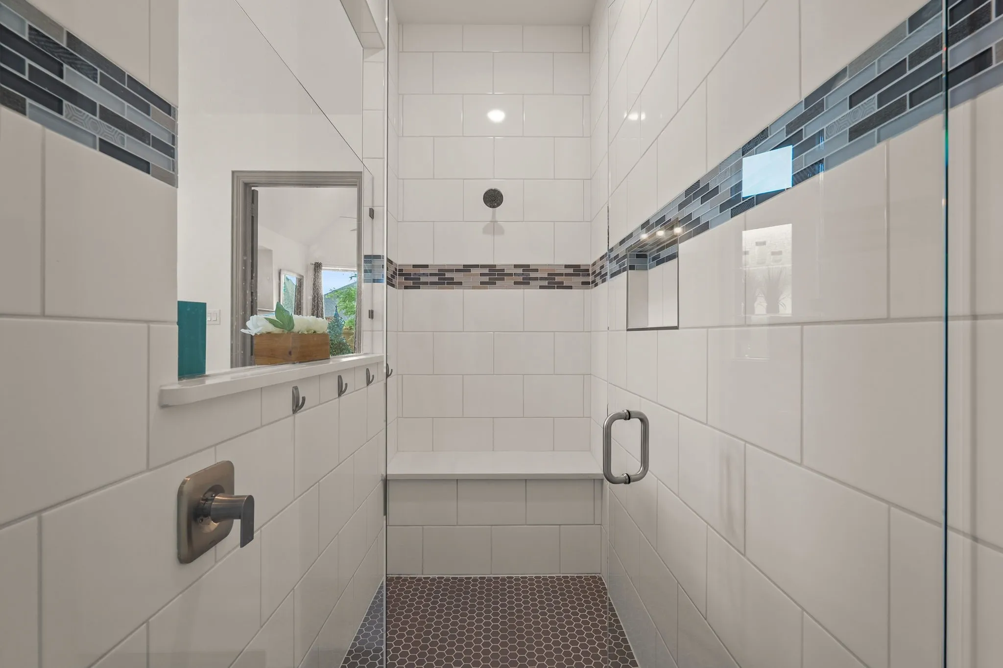 Contemporary shower enclosure featuring white subway tile, mosaic accent bands, a built-in bench, a recessed niche, and a contrasting penny tile floor