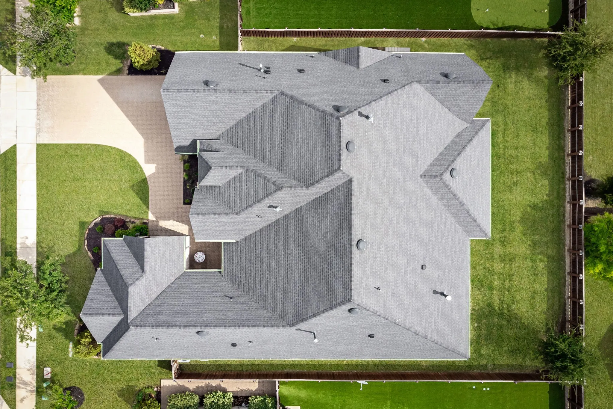 Expansive property featuring a multi-gabled roofline, a concrete driveway, perimeter fencing, and mature landscaping