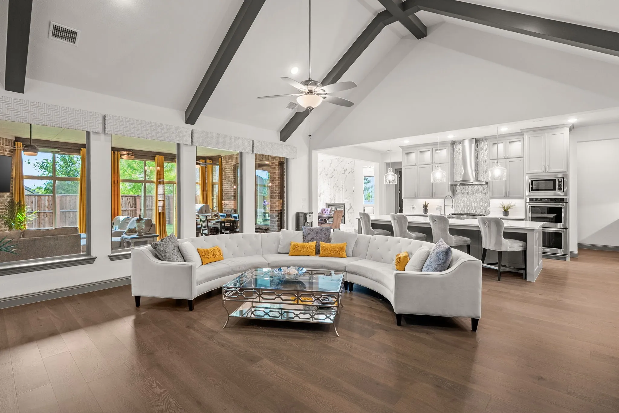 Spacious living area featuring high vaulted ceilings with exposed beams, wood-finish flooring, and multiple large windows