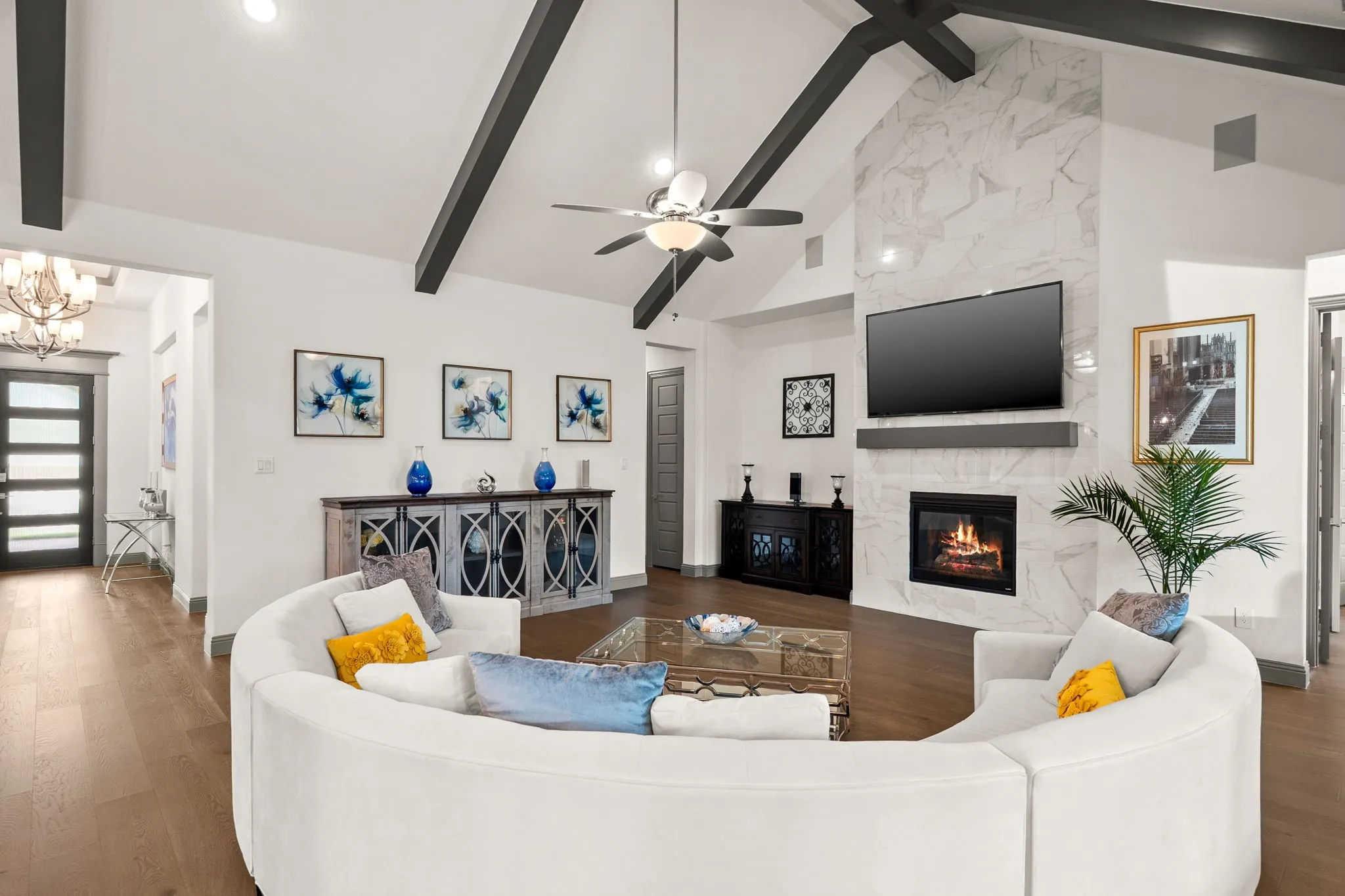 Vaulted ceilings with exposed dark beams, a floor-to-ceiling fireplace with a stone surround, and wood-finish flooring