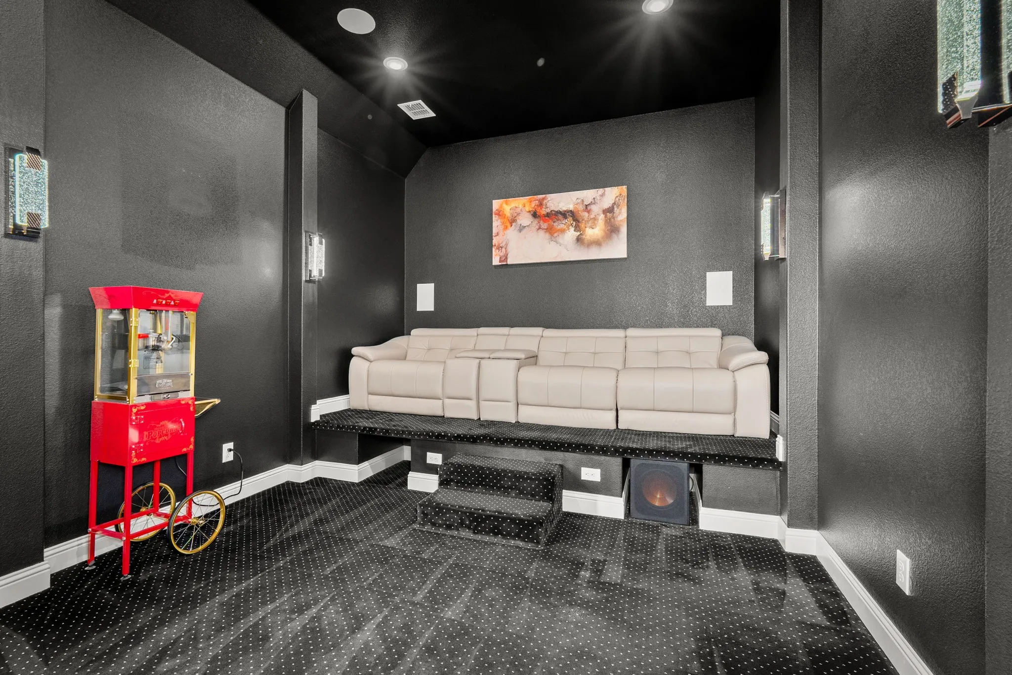 Dedicated media room featuring tiered seating, dark walls, and ceiling-mounted recessed lighting