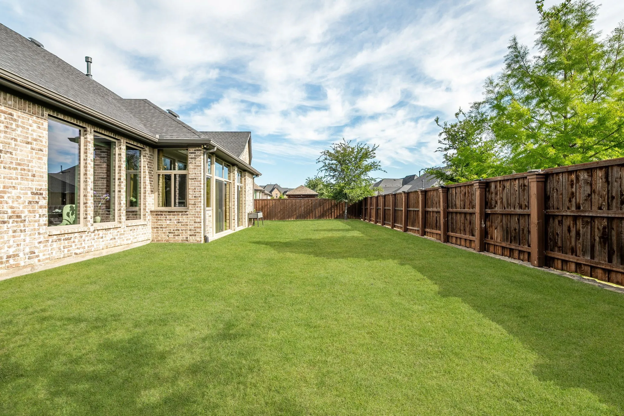 Expansive backyard with a manicured lawn, full privacy fencing, and a brick exterior featuring multiple large windows and a glass sliding door