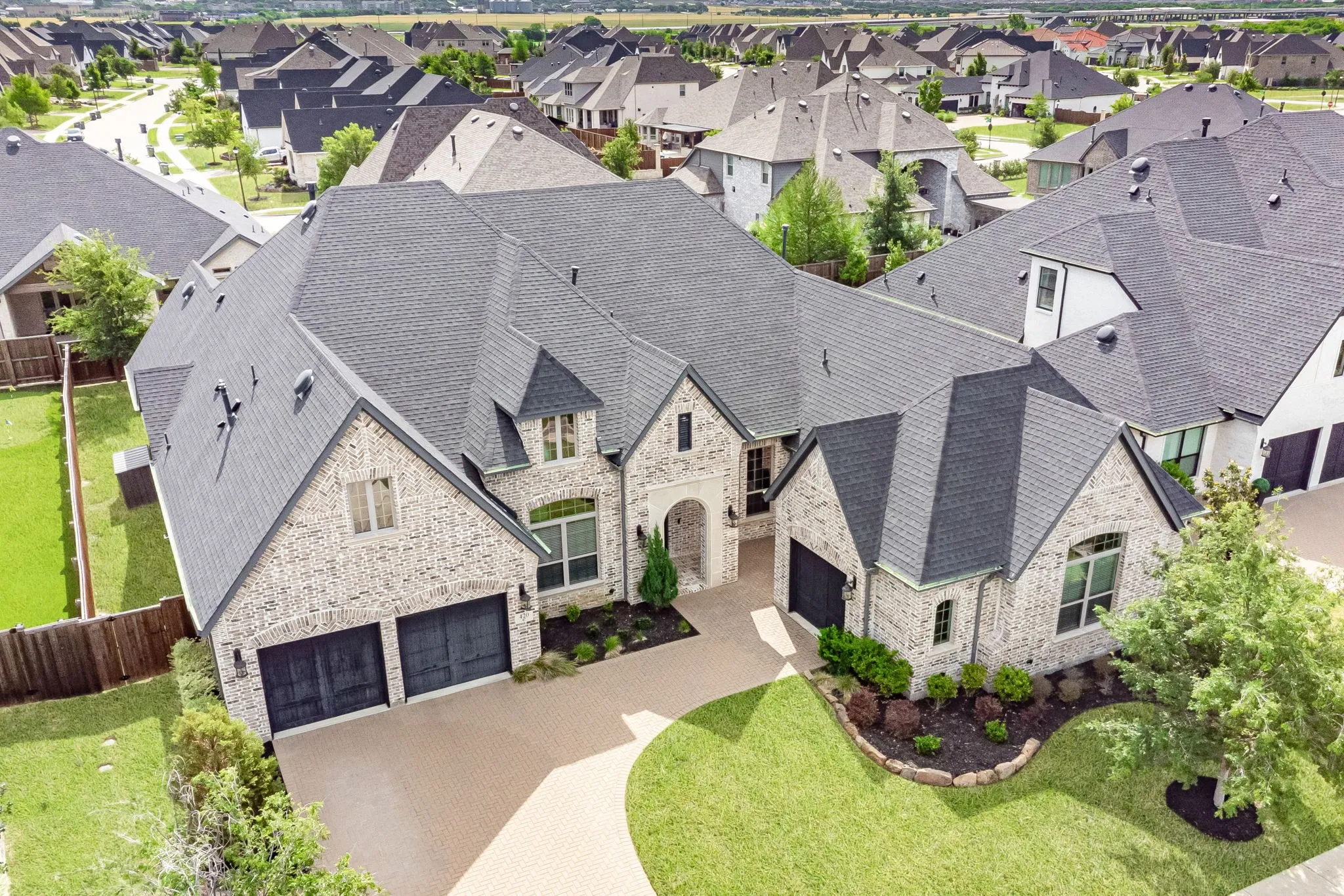 Traditional-style residence featuring a light-colored brick exterior, dark shingle roofing, and multiple gables