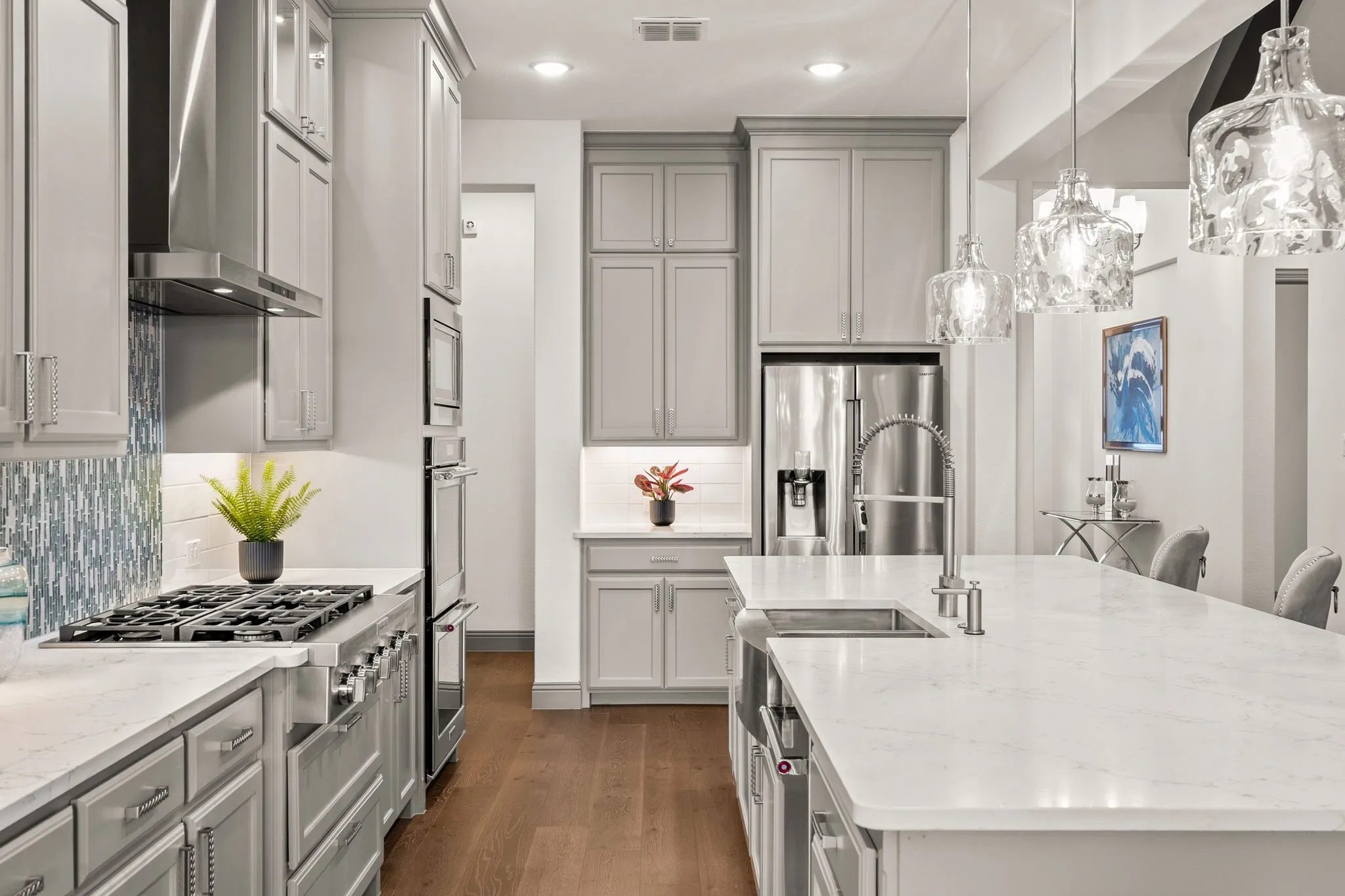 Gourmet kitchen featuring a large island with an undermount sink, pendant lighting, stainless steel appliances, a five-burner gas range with a matching range hood, and a blue-toned mosaic tile backsplash