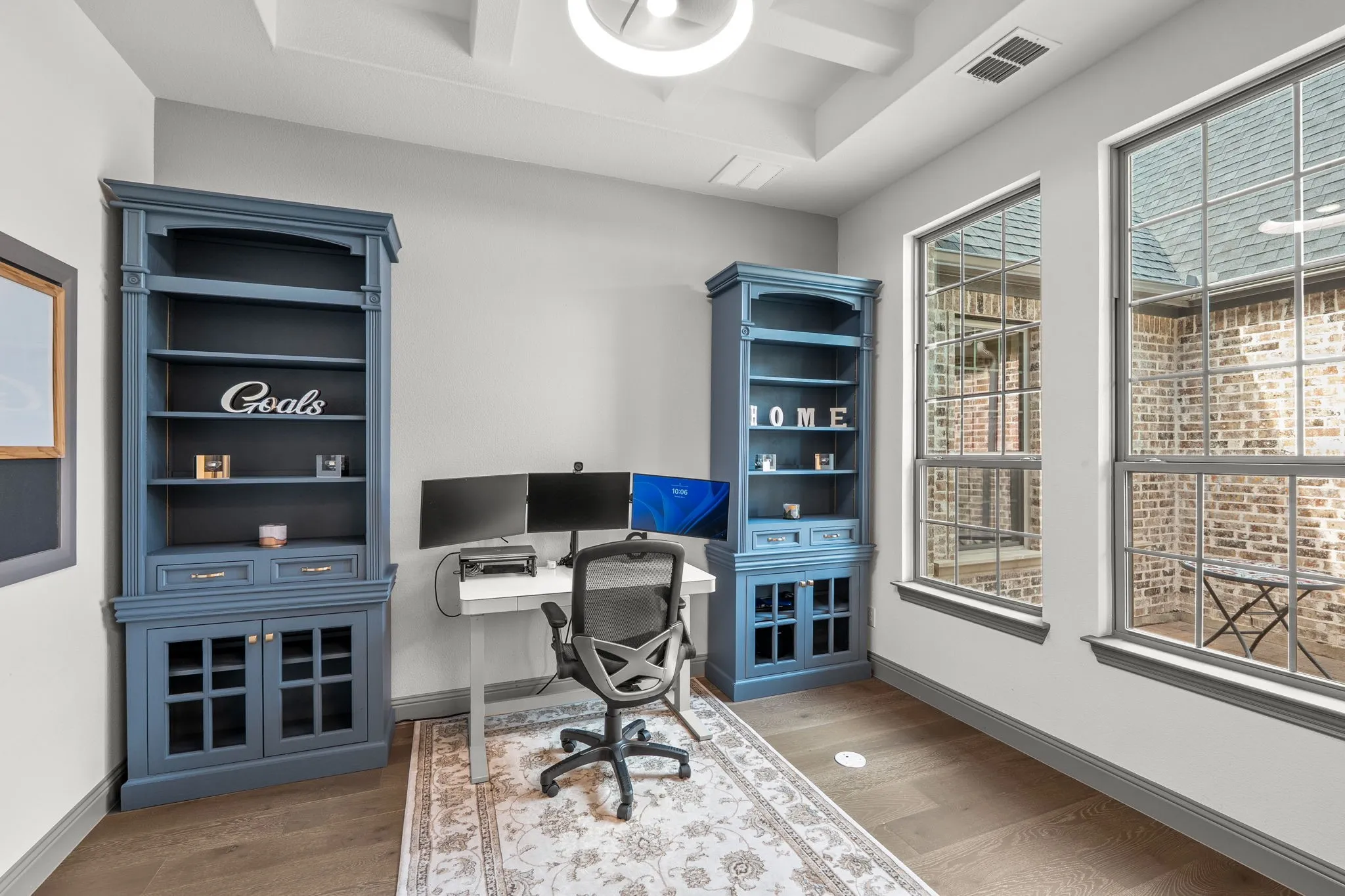 Dedicated space featuring two built-in bookcases, two large windows with grid patterns, wood-finish flooring, and a tray ceiling