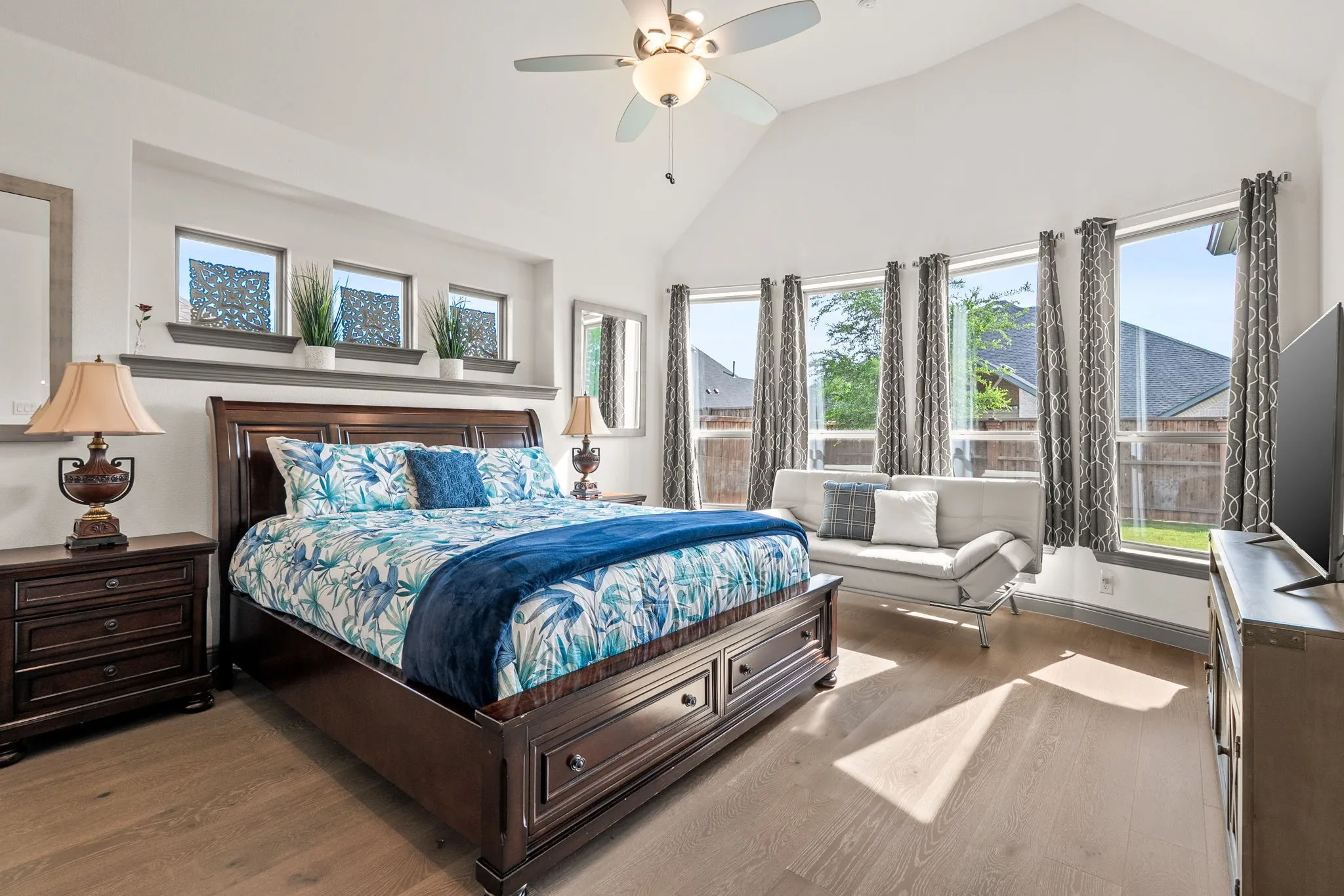 Vaulted ceiling bedroom featuring five large windows, a ceiling fan with integrated lighting, a recessed wall niche, and wood-finish flooring