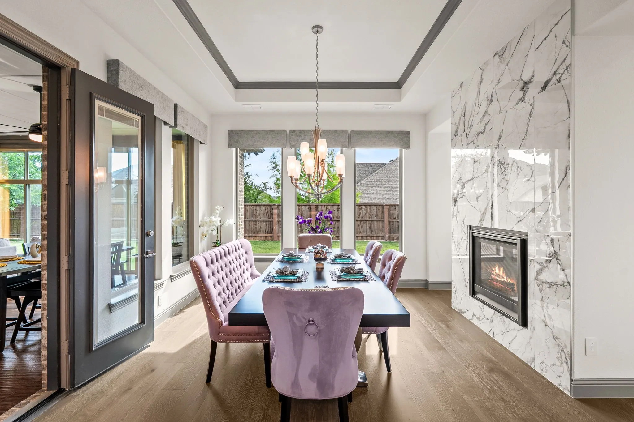 Dining room featuring a marble-patterned fireplace, tray ceiling, wood-finish flooring, and a glass-paneled door