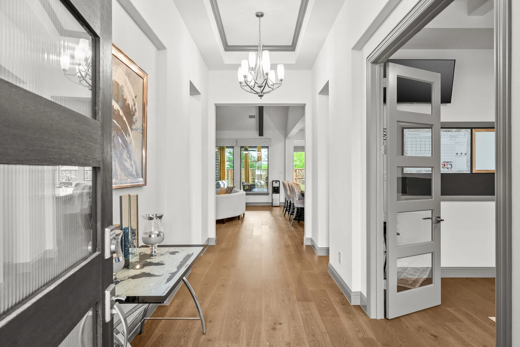 Entryway featuring wood-finish flooring, a modern black door with frosted glass panels, and a coffered ceiling with two contemporary chandeliers