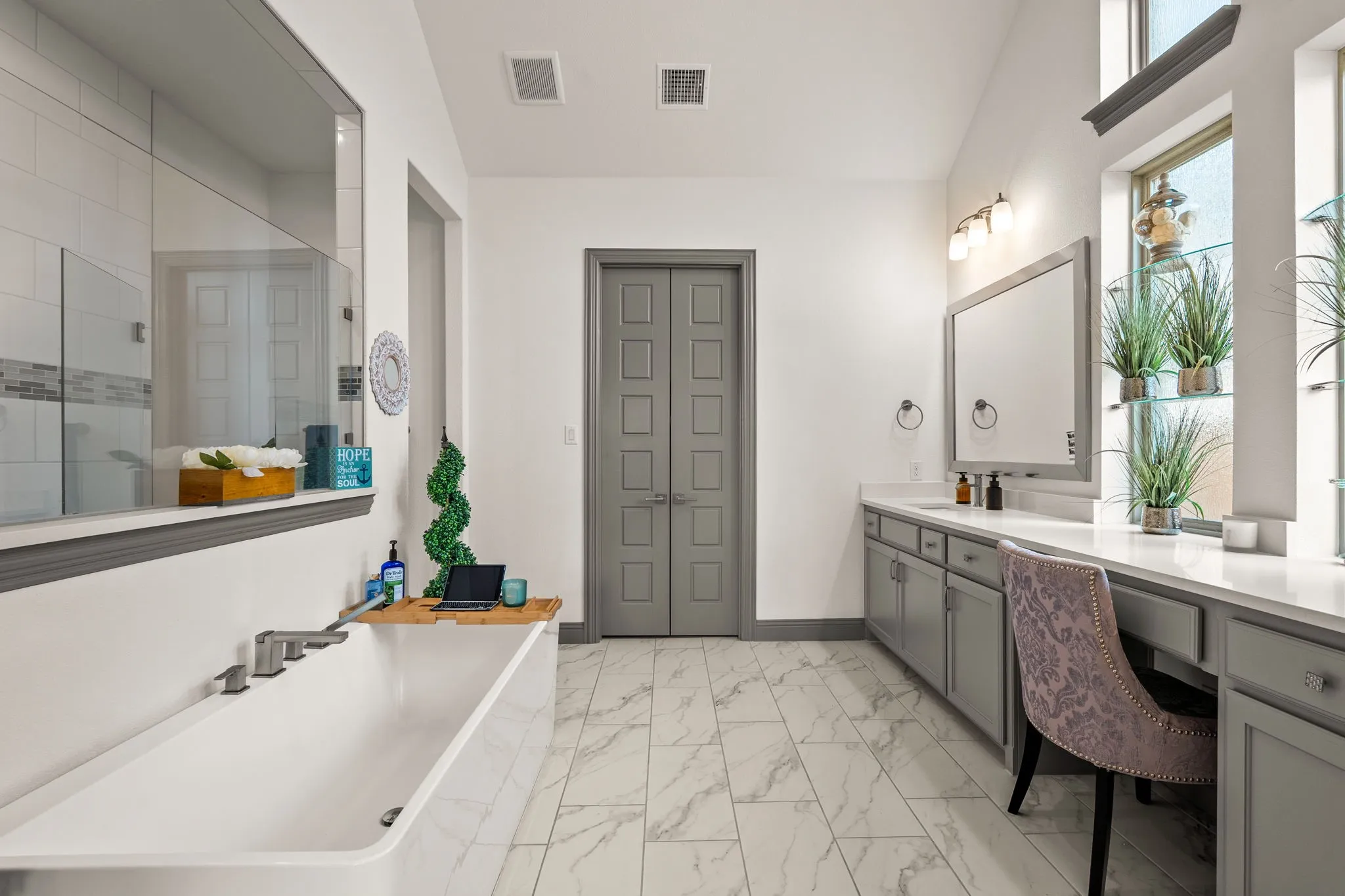 Spacious bathroom featuring a freestanding soaking tub, walk-in shower with glass enclosure, dual vanity with undermount sinks, dedicated vanity area, and marble-look flooring