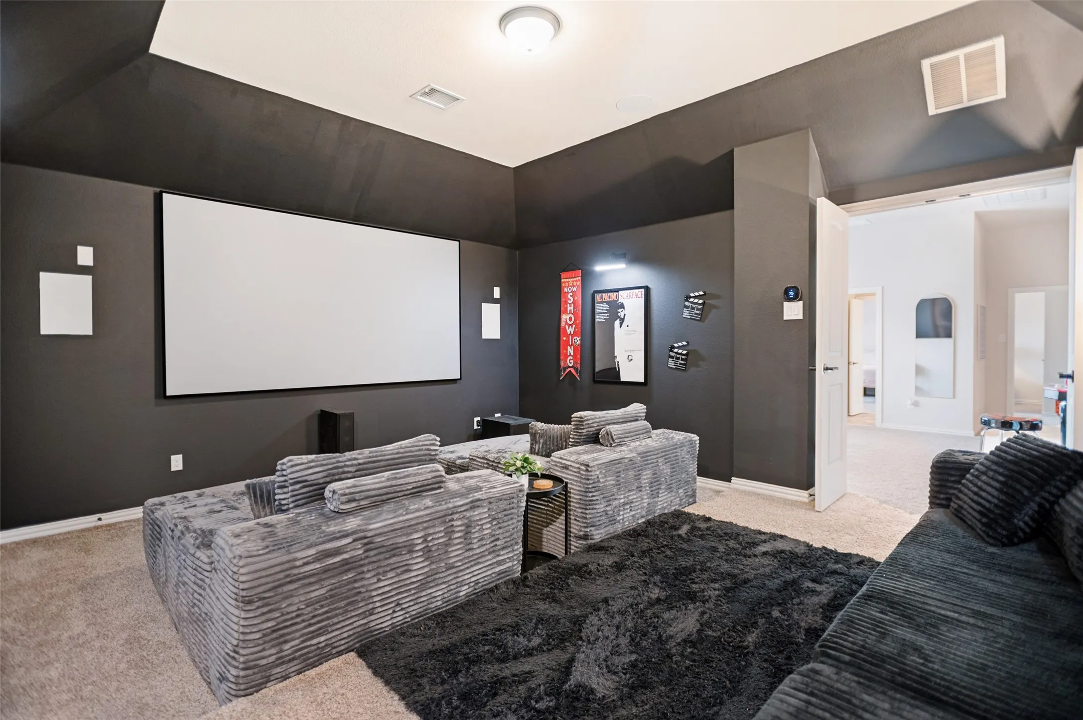 Dedicated media room featuring a large projection screen, dark wall finishes, and recessed lighting