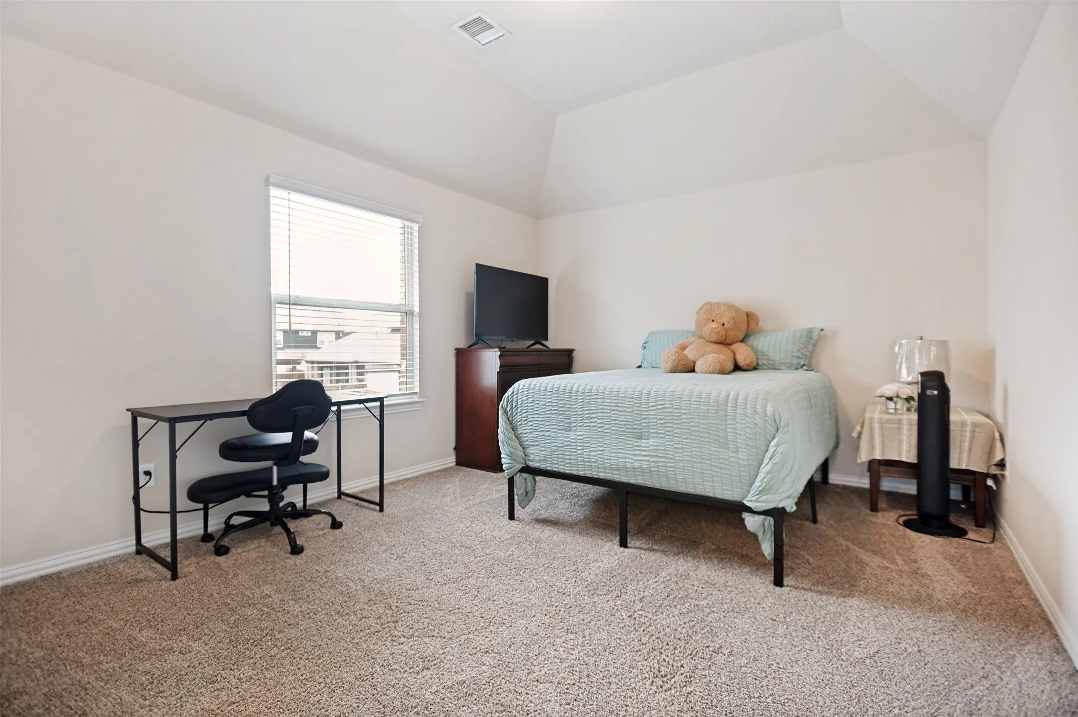Carpeted bedroom featuring a vaulted ceiling and a single window with blinds