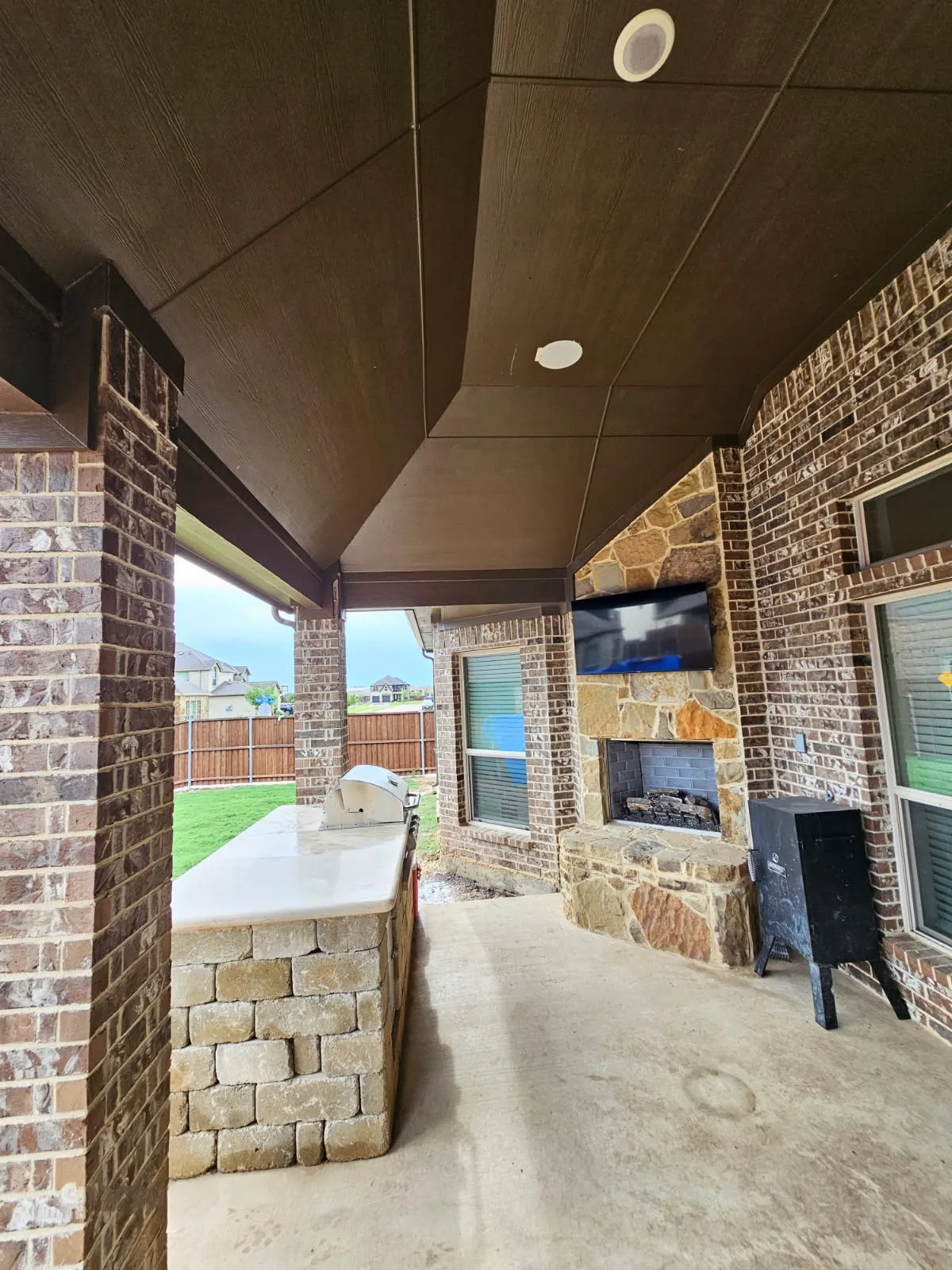Covered patio featuring an outdoor kitchen with built-in grill, a stone fireplace, and brick columns
