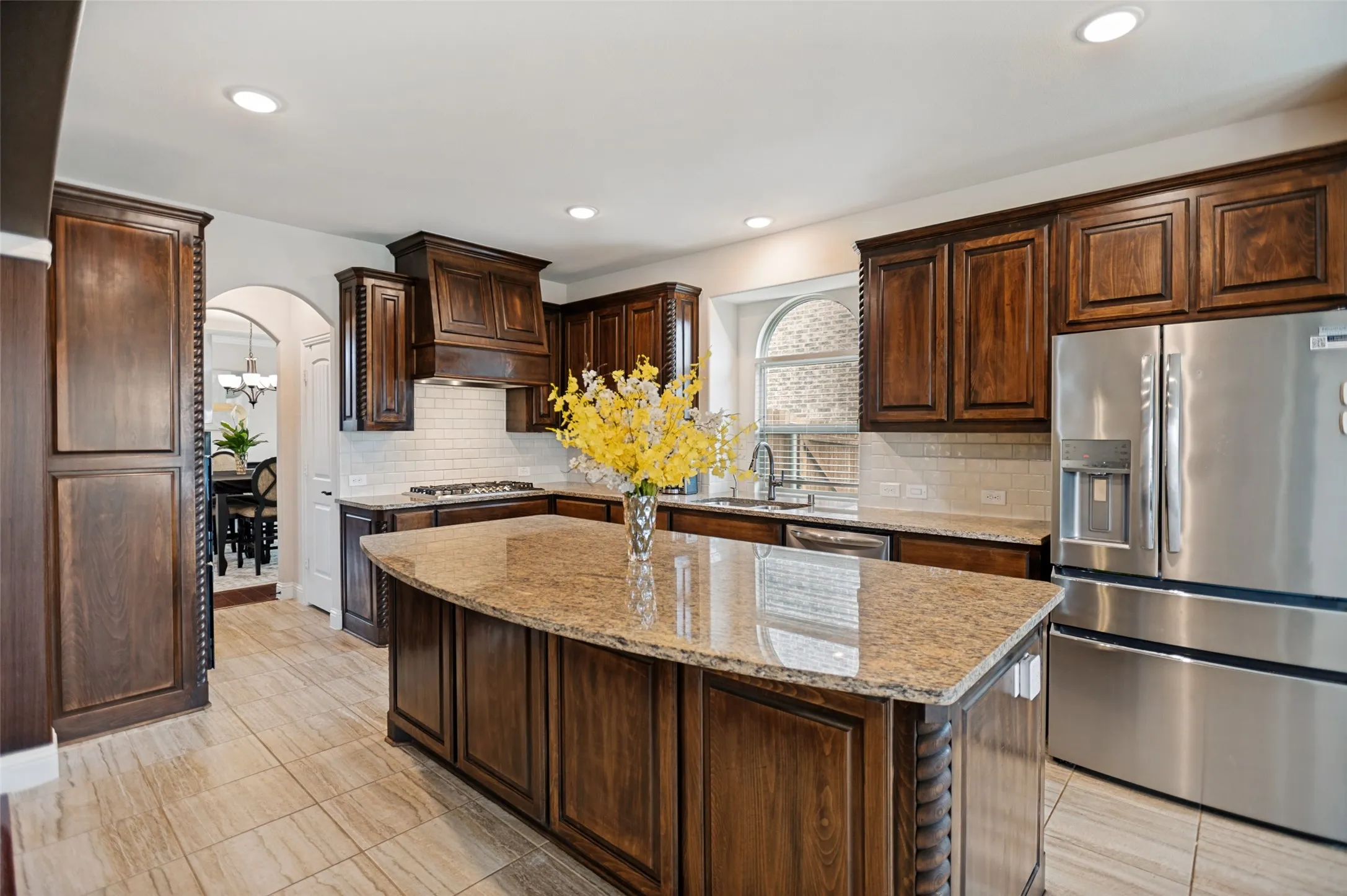 Kitchen featuring dark wood cabinetry, a central island with a stone countertop, stainless steel appliances, a tile backsplash, and recessed lighting