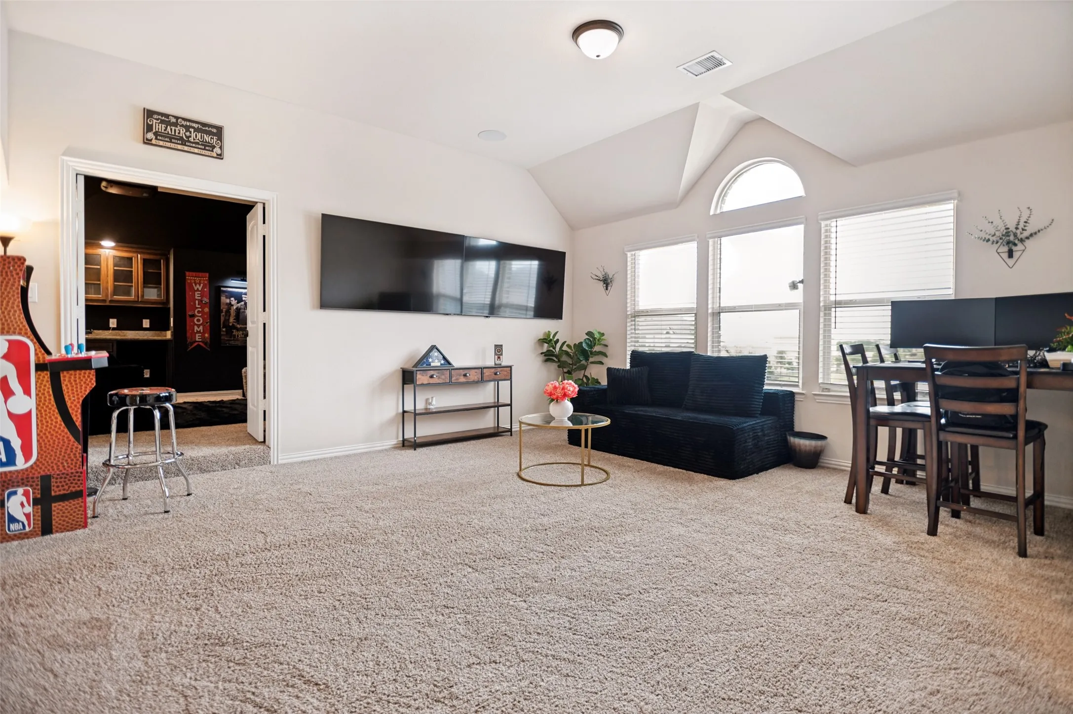Spacious upstairs family room with vaulted ceilings, a large arched window, neutral carpet, and a recessed area already plumbed for a future wet bar.