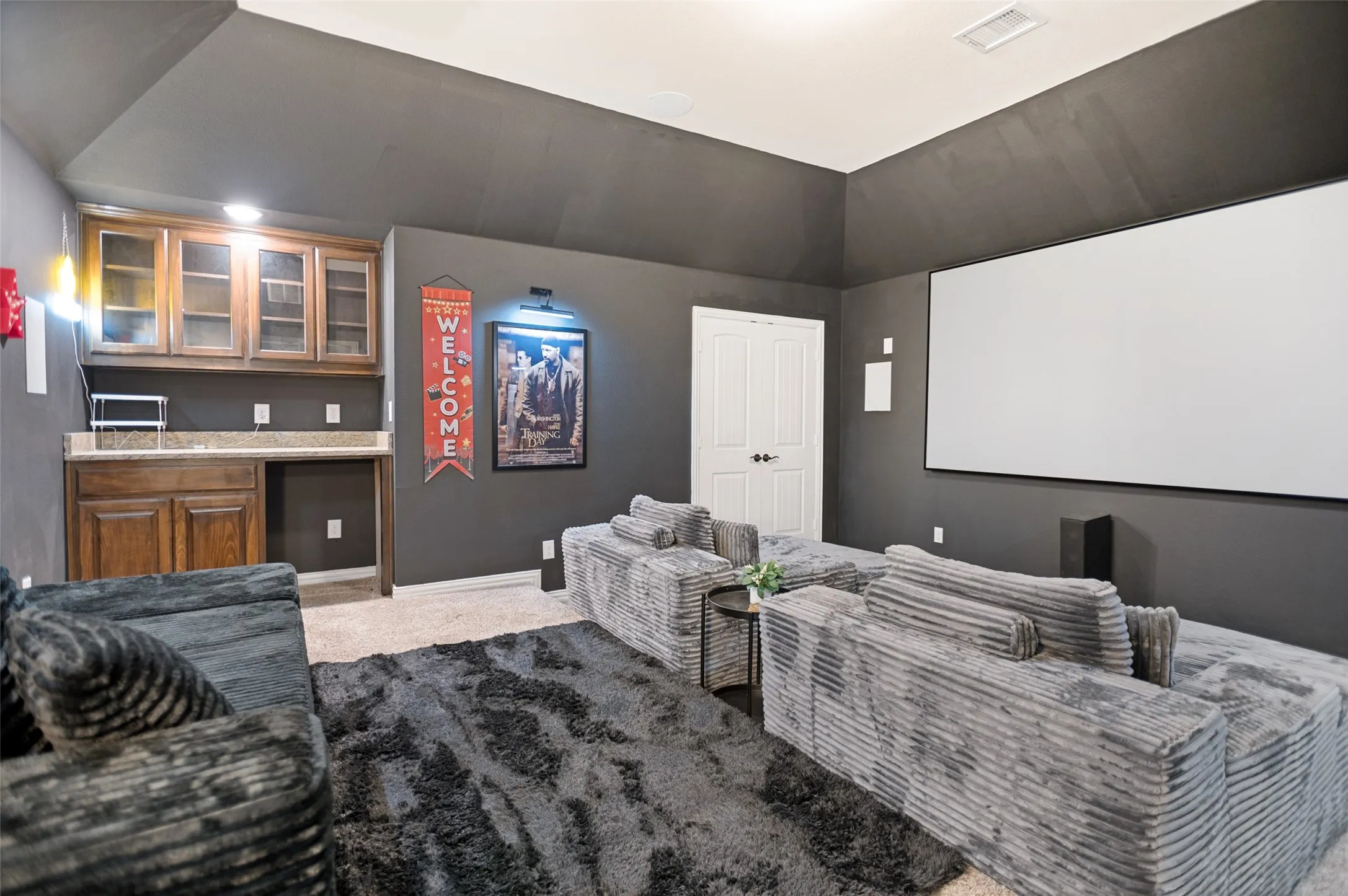 Dedicated media room featuring a large projection screen, dark wall finishes, and recessed lighting