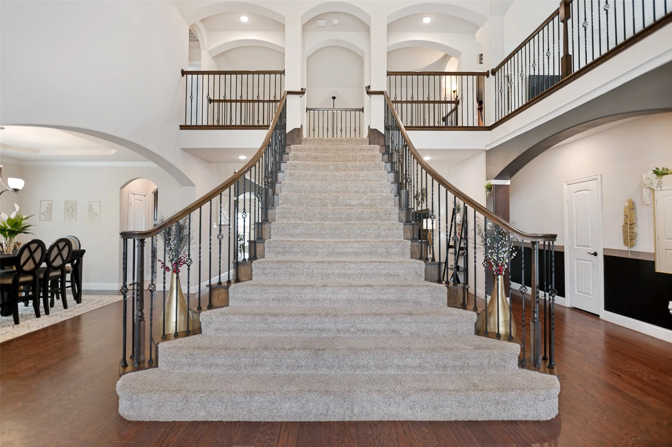 Grand straight staircase with flared wrought iron railing and wood handrails.