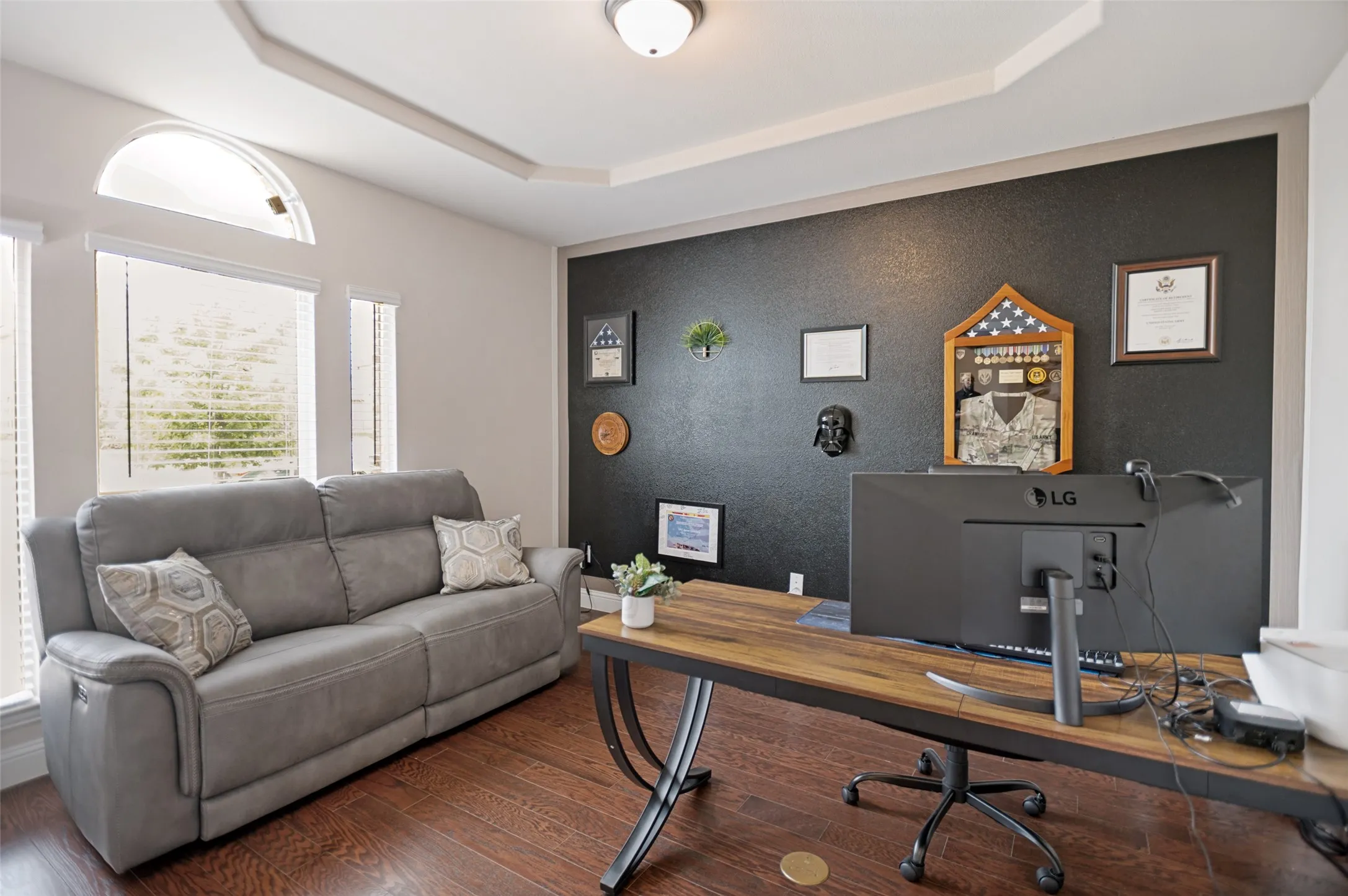Spacious office featuring wood-finish flooring, a tray ceiling, and an accent wall