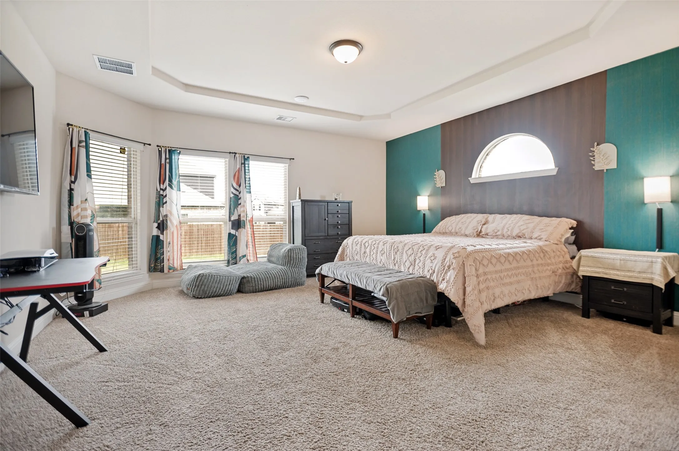 Generously sized primary bedroom with a tray ceiling, abundant natural light, neutral carpet, and a distinctive arched transom window accent.
