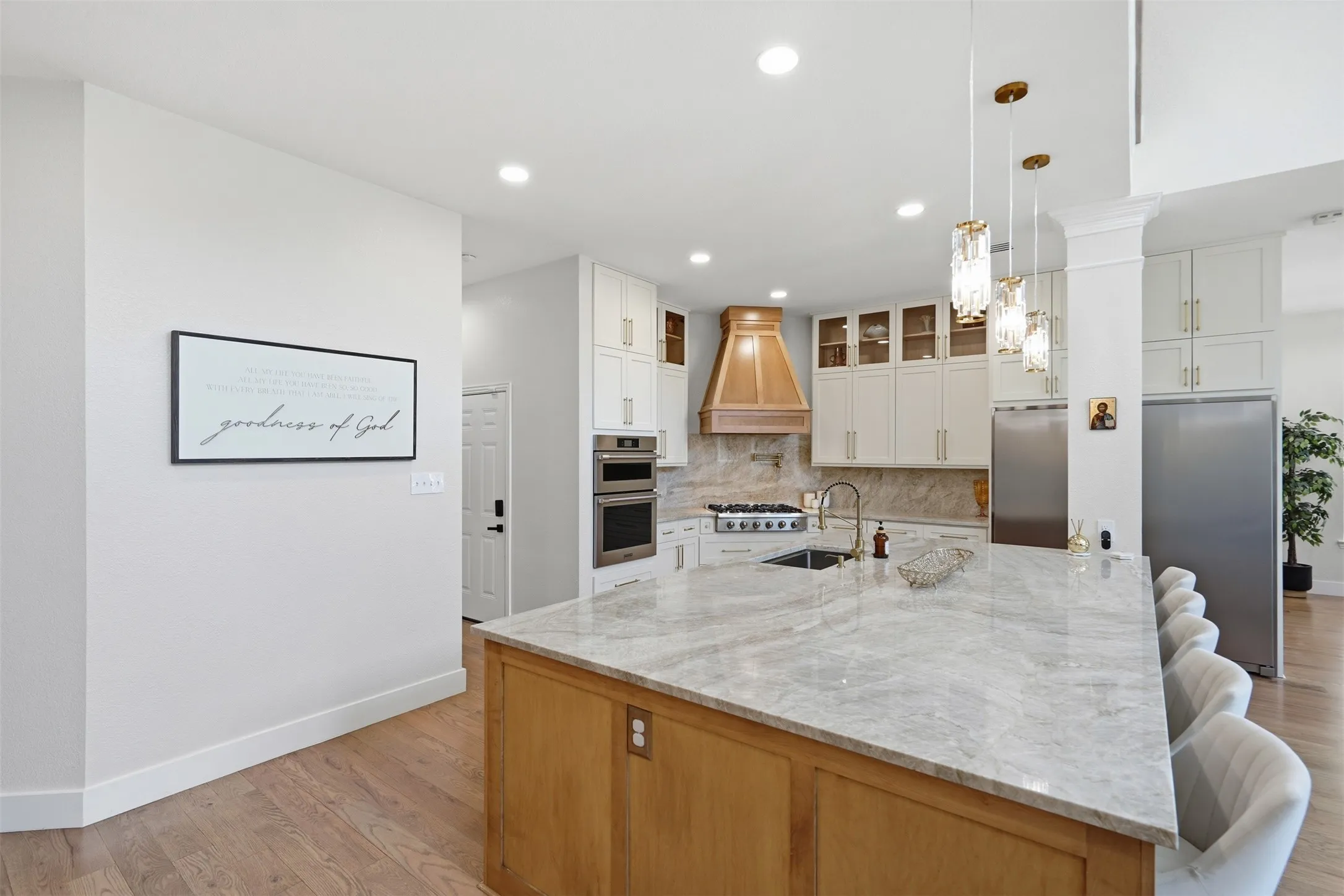 Expansive kitchen island with a stone surface and built-in sink, wood-finish cabinetry, stainless steel appliances, and pendant lighting