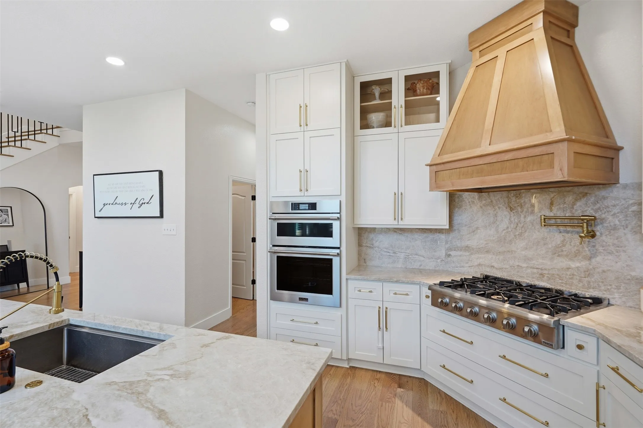 White shaker cabinetry, stainless steel appliances, a pot filler, wood-finish flooring, and recessed lighting
