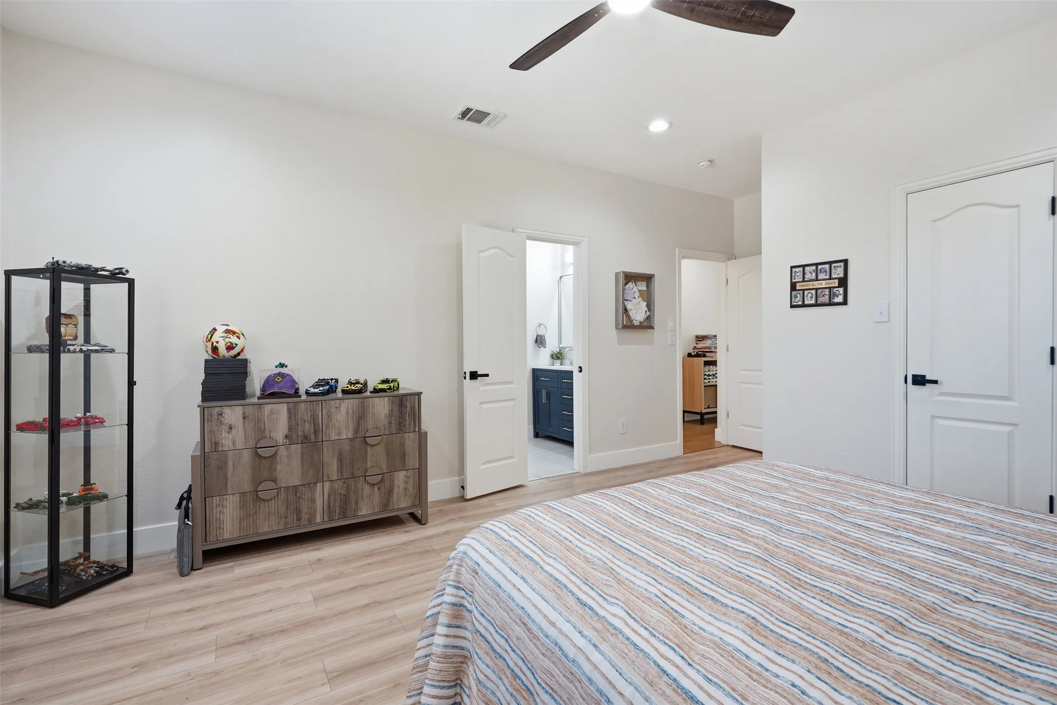 Wood-finish flooring, recessed lighting, ceiling fan, white paneled doors, and access to an en-suite bathroom featuring a vanity with a blue finish