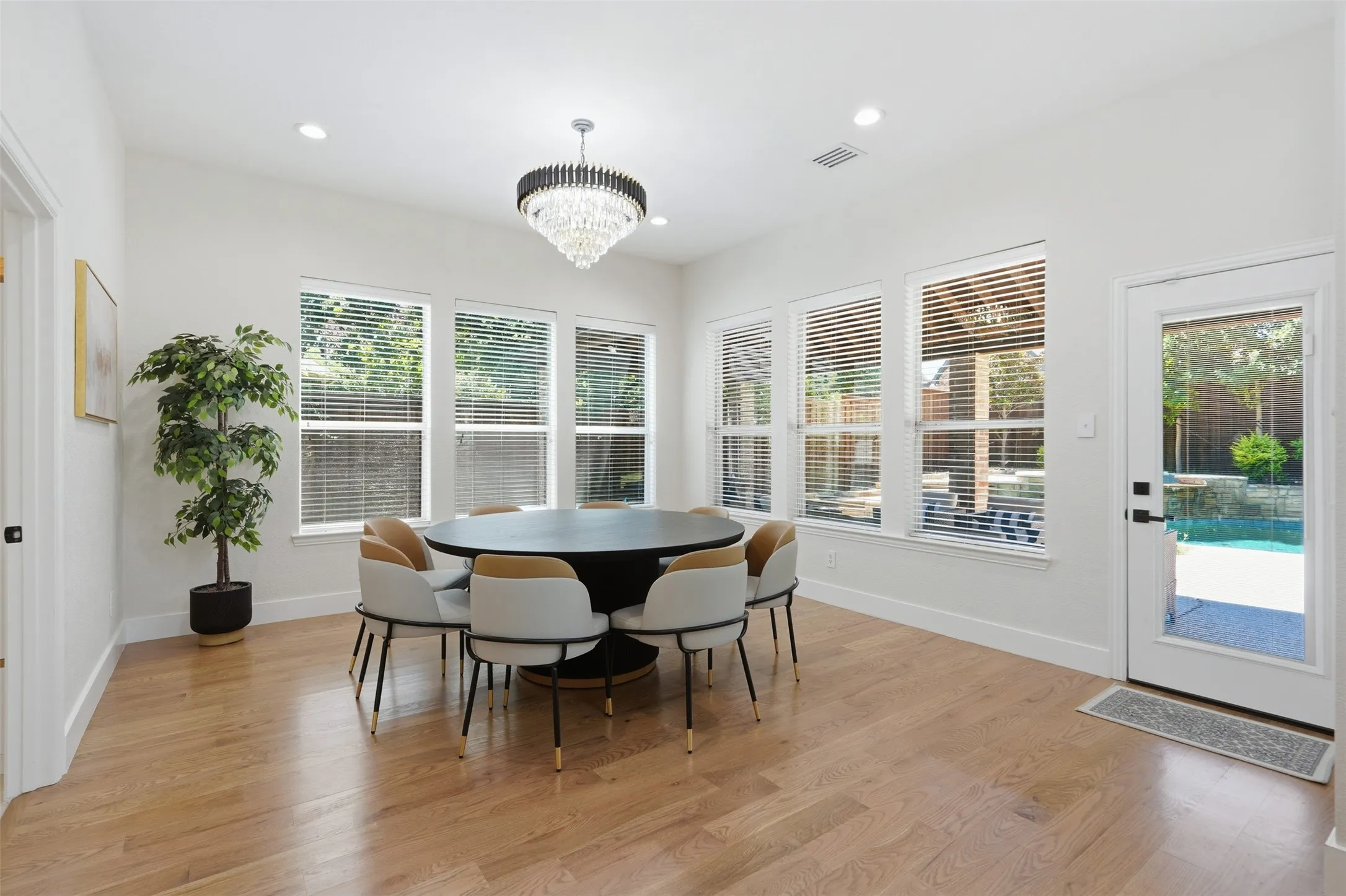 Wood-finish flooring, recessed lighting, multiple windows with blinds, a crystal chandelier, and a glass-paneled door