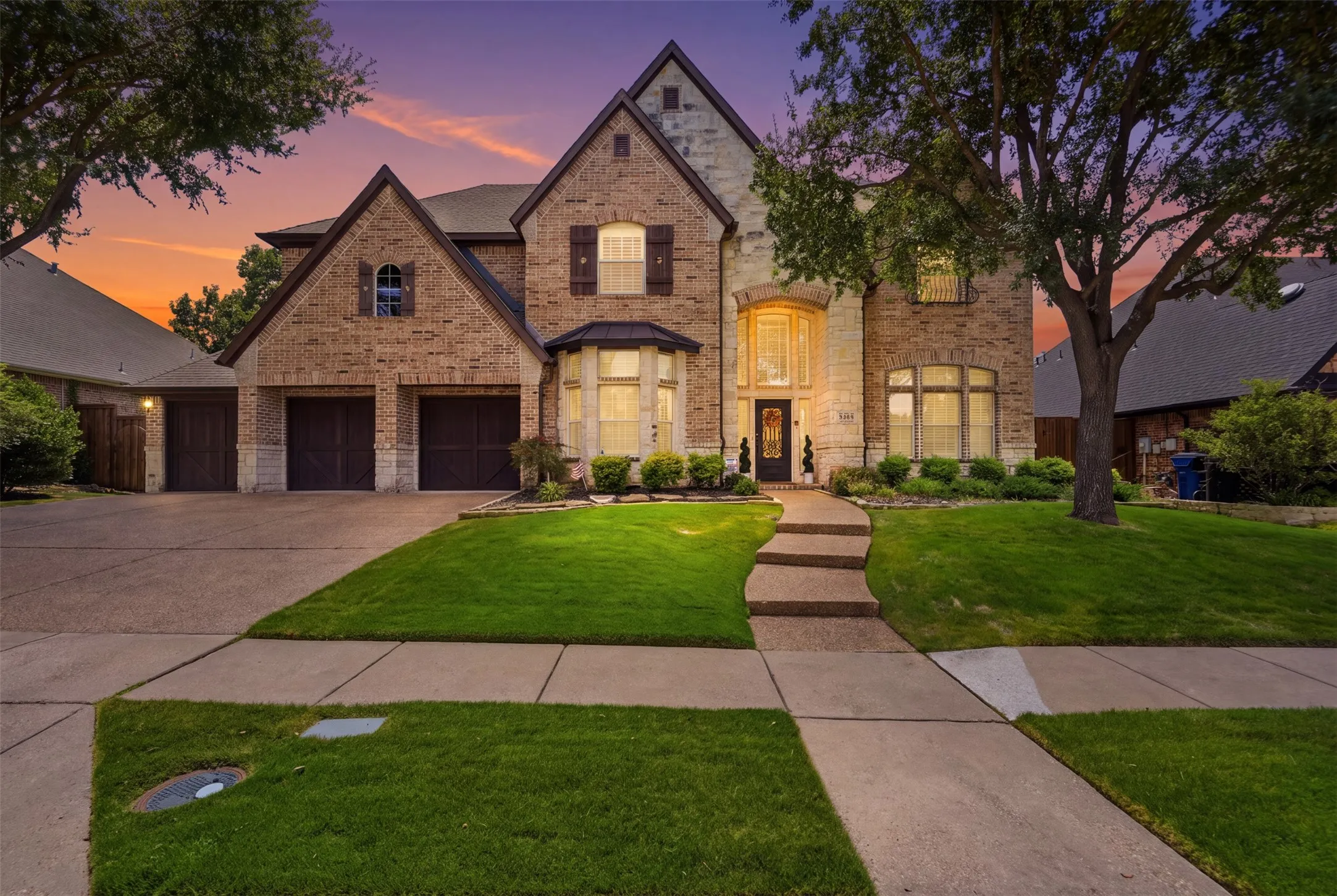 Stone and brick facade with multiple gables, three-car garage, established front landscaping, and a concrete paver walkway