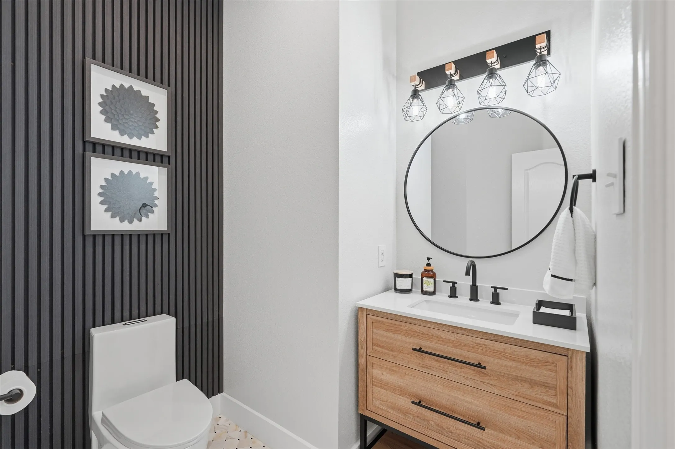 Powder room featuring a wood-finish vanity with a white countertop and undermount sink, a circular mirror, and matte black fixtures