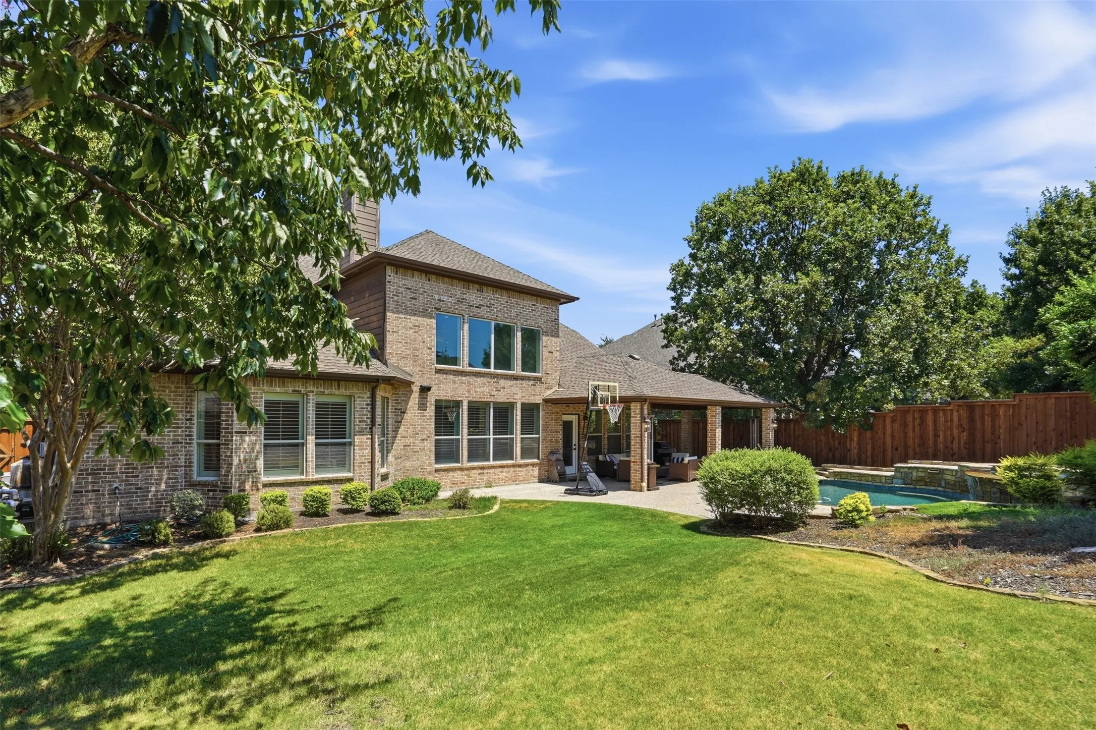 Brick exterior, covered patio, integrated swimming pool, manicured lawn, and privacy fencing