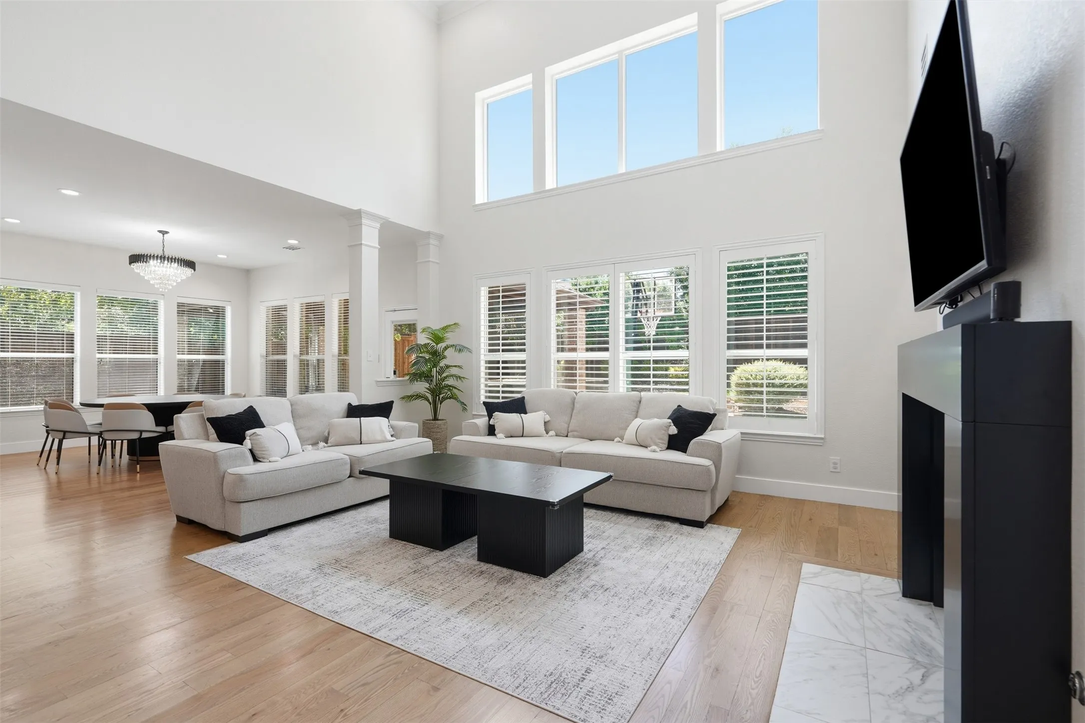 Two-story living area featuring wood-finish flooring, a modern fireplace with a marble-style hearth, and high ceilings