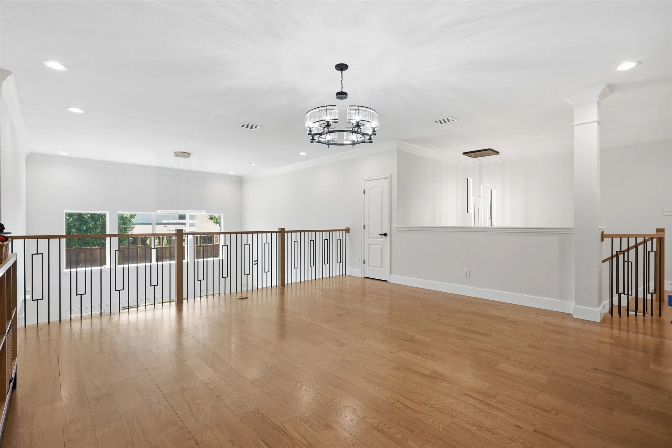 Hardwood flooring, contemporary chandelier, recessed lighting, white walls, and decorative metal railings