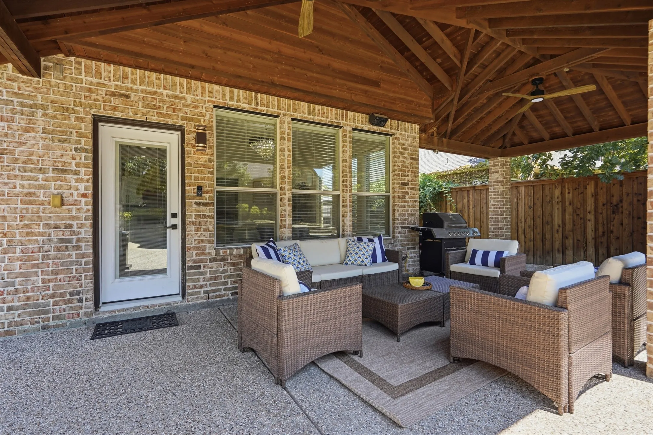 Expansive covered patio featuring a vaulted wood ceiling, dual ceiling fans, brick exterior, and a privacy fence