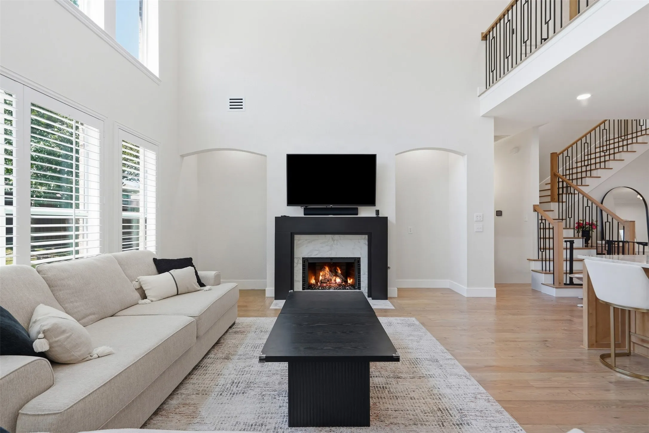 Double-height ceiling, fireplace with stone surround, hardwood flooring, and a balustrade staircase with wood and metal railing