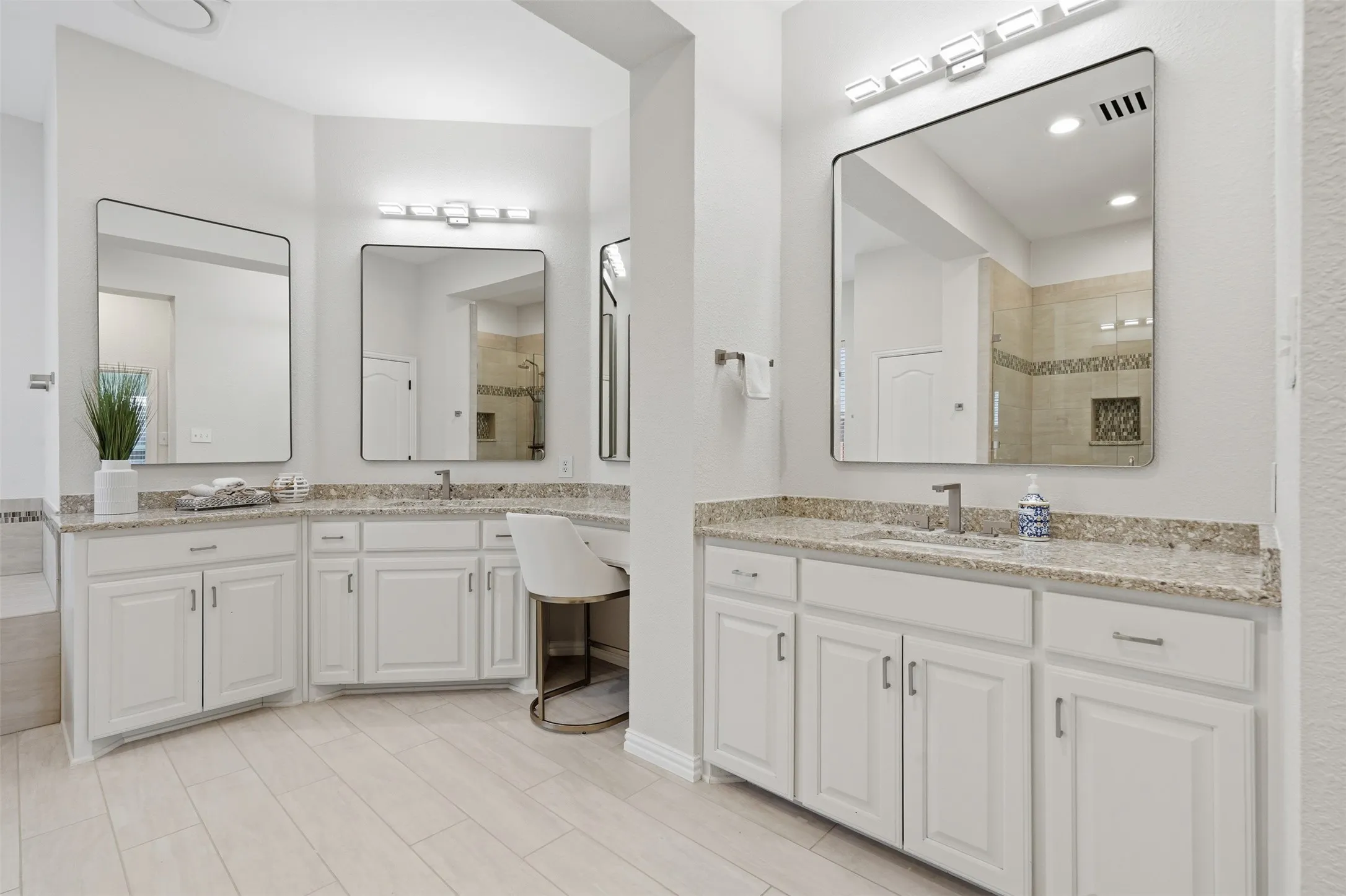 Dual vanities with undermount sinks, granite countertops, white cabinetry, and wall-mounted mirrors